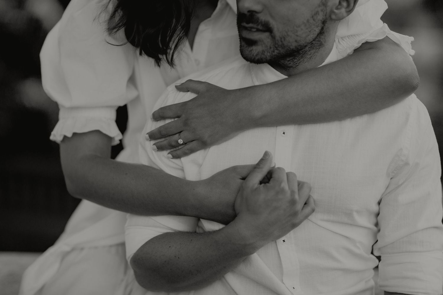 Black and white close-up of a couple embracing, showing an engagement ring on her hand.