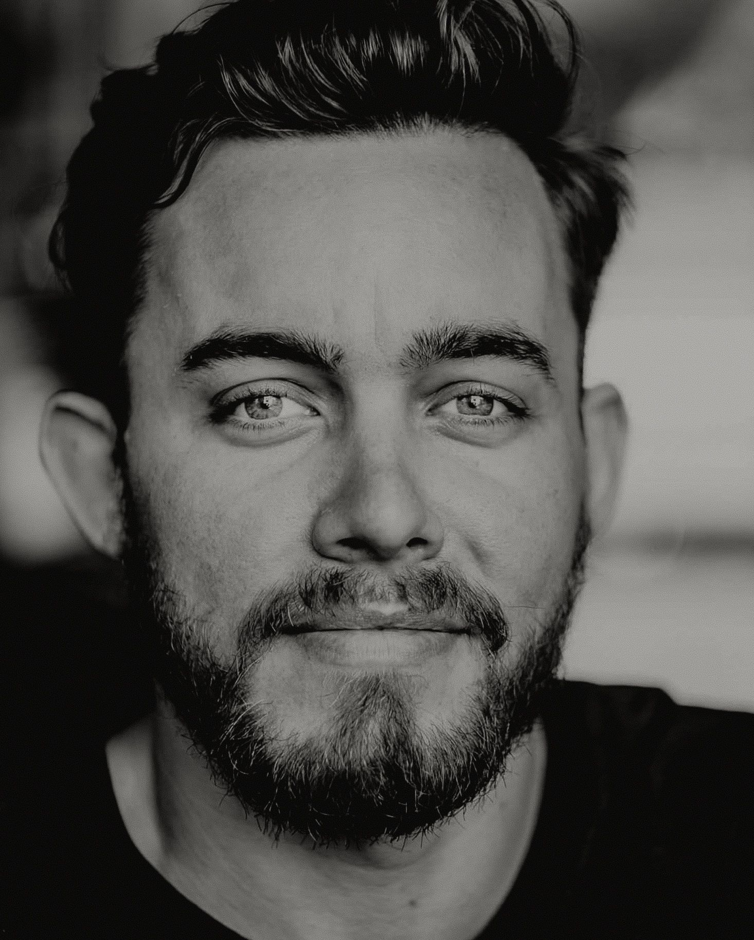 Close-up black and white portrait of bearded man with light eyes and dark hair.
