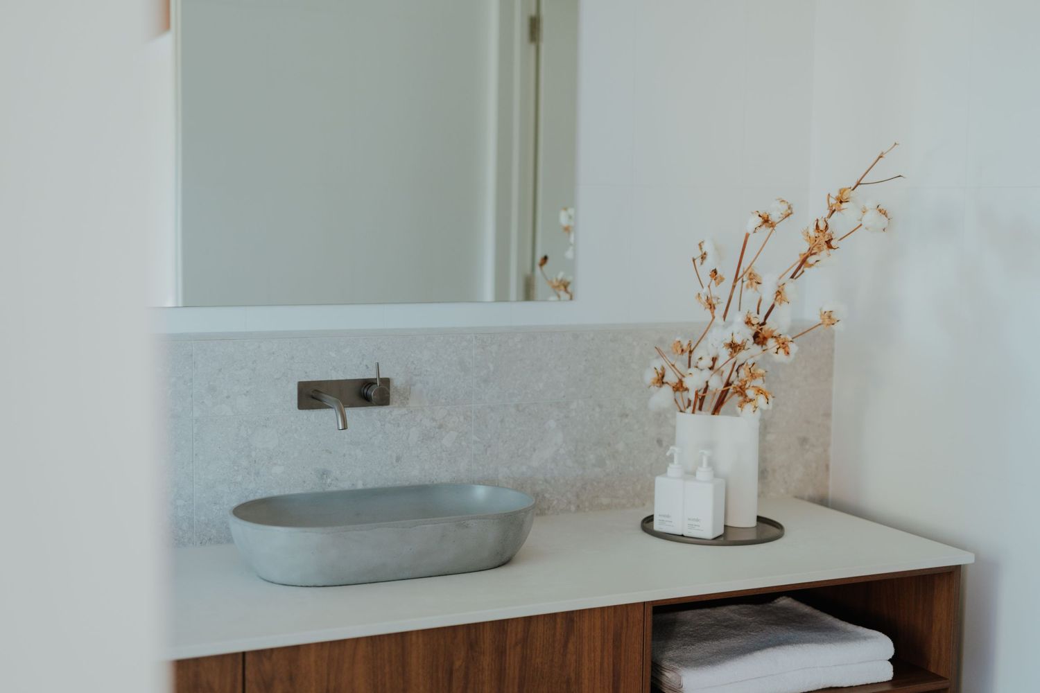 Modern bathroom vanity with stone basin, marble mosaic splashback, timber cabinet and dried floral arrangement.