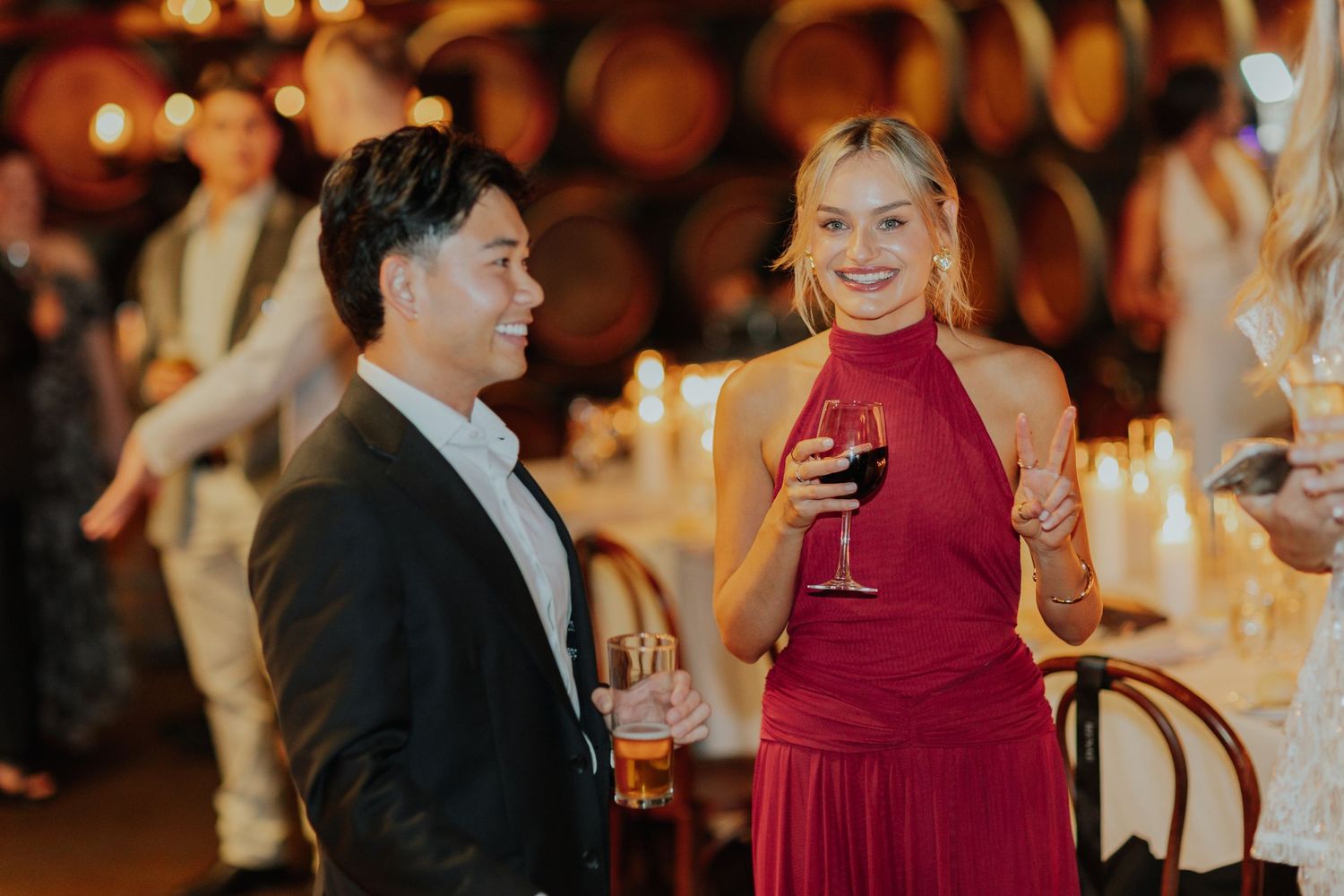 Man and woman in formal attire enjoying red wine at a winery barrel room event.