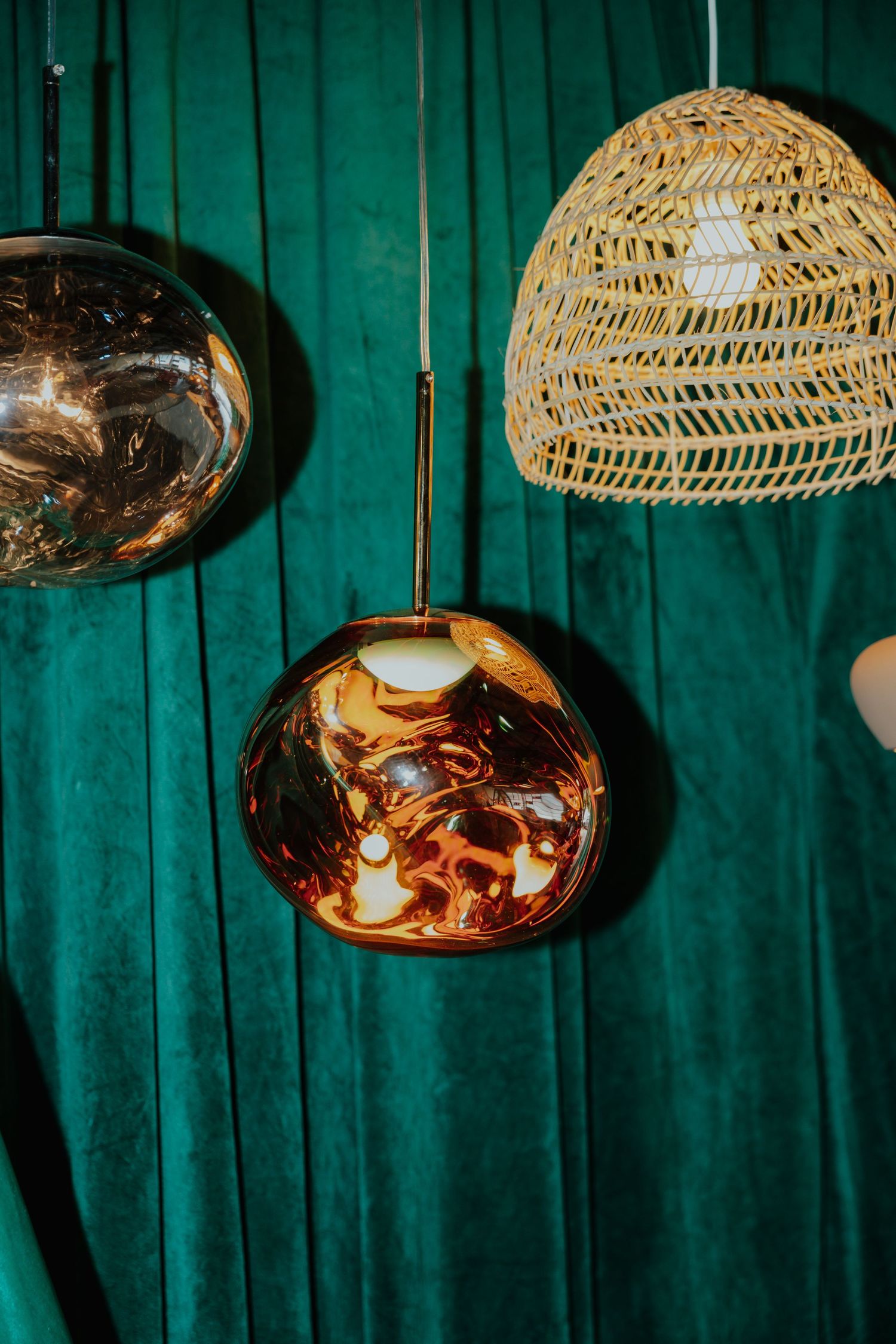 Close-up of amber glass globe and wicker pendant lights hanging against a rich green velvet curtain backdrop.