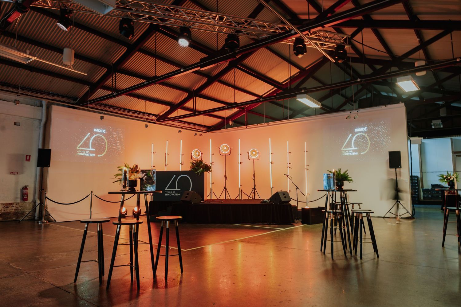 Spacious event venue with stage setup, candles, projections and bar tables for a 40th anniversary.