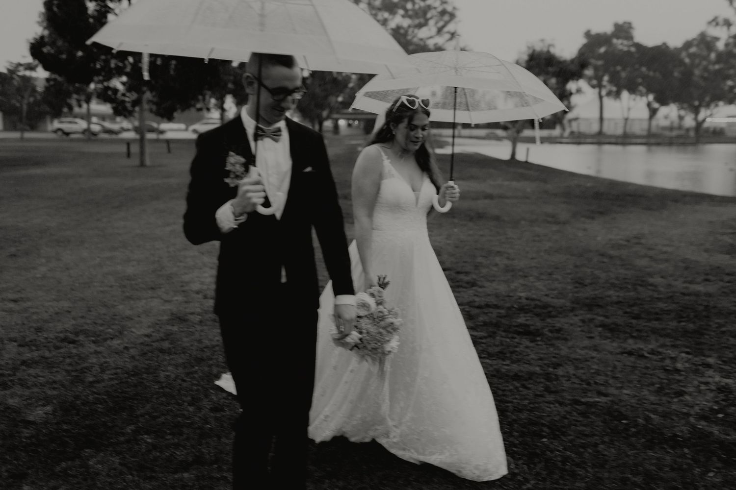 Black and white photo of bride and groom walking with umbrellas.
