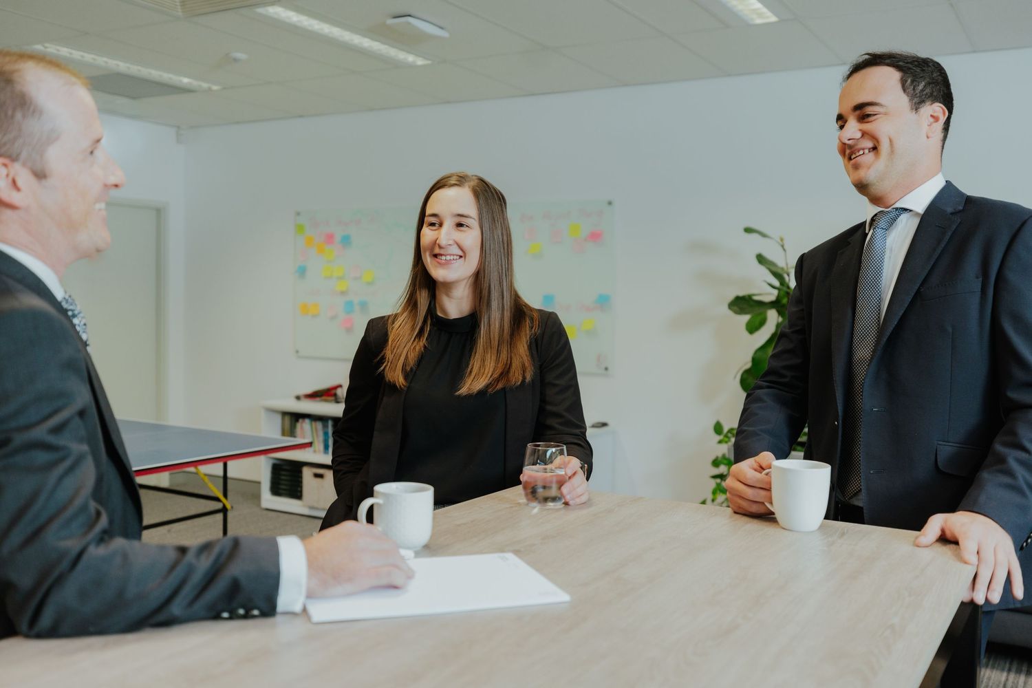 Three business professionals having a standing meeting around a table in a bright modern office.