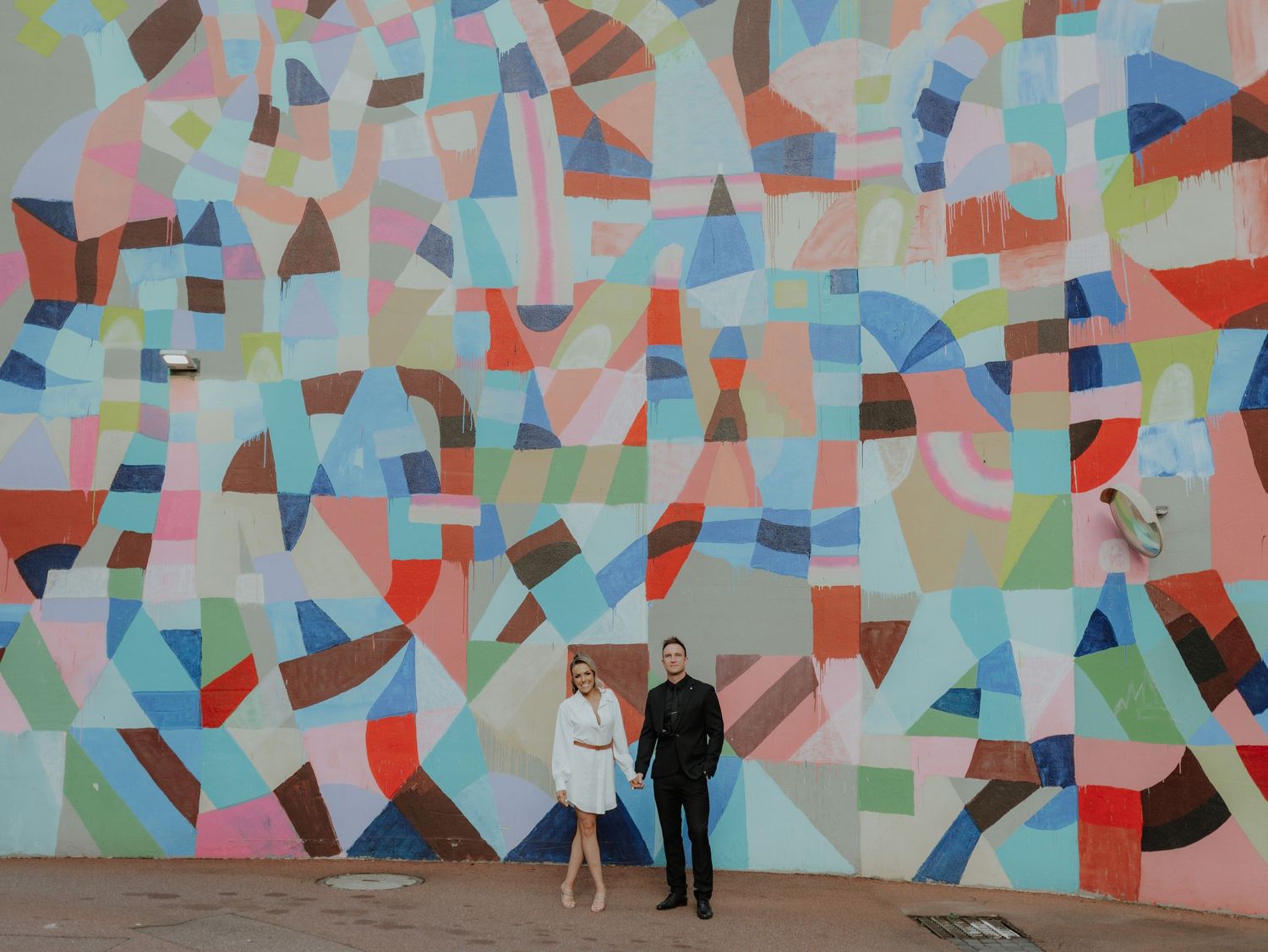 Couple standing before vibrant geometric colorful mural wall in urban setting.