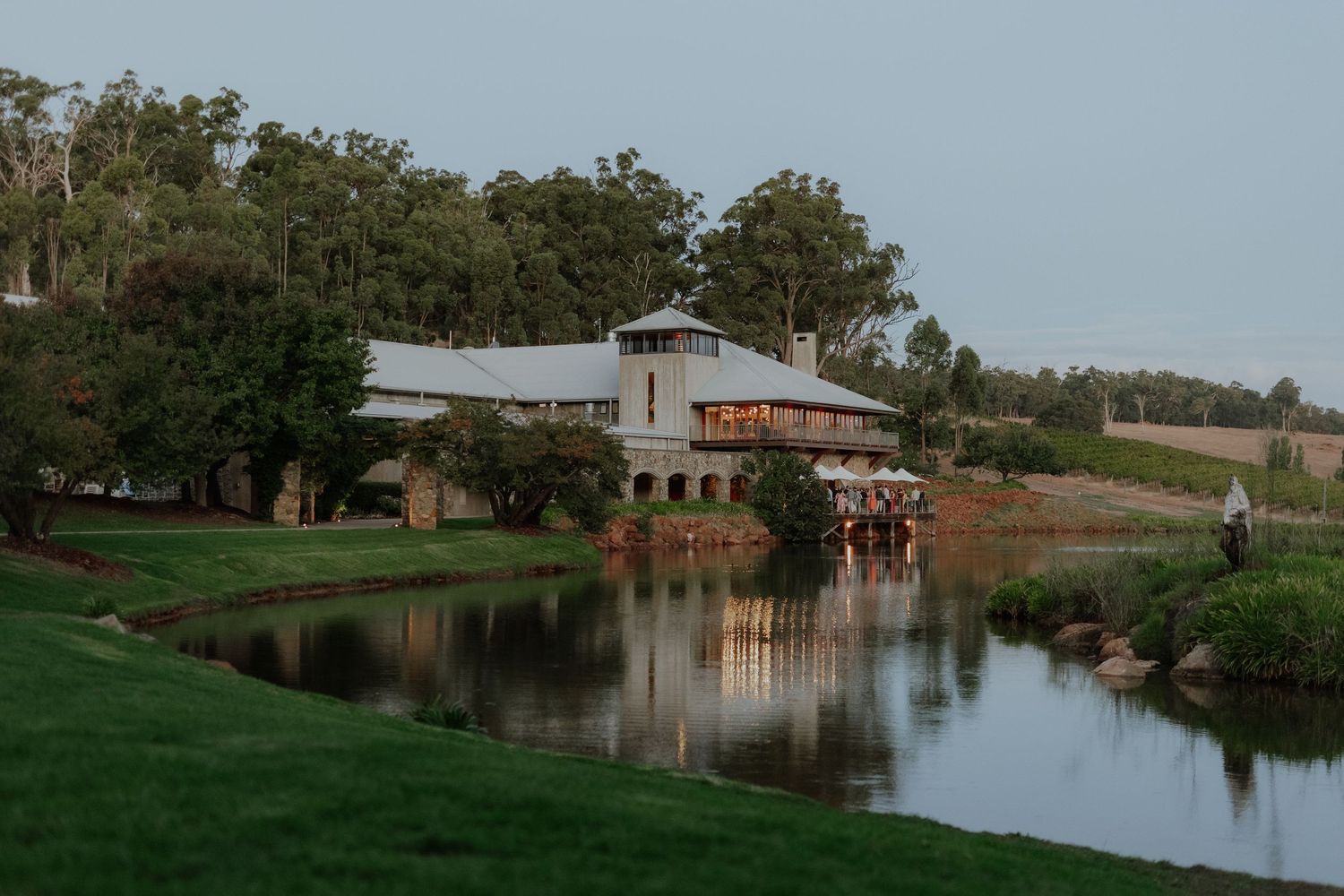 Elegant wedding venue reflected in a serene pond at dusk surrounded by lush greenery.