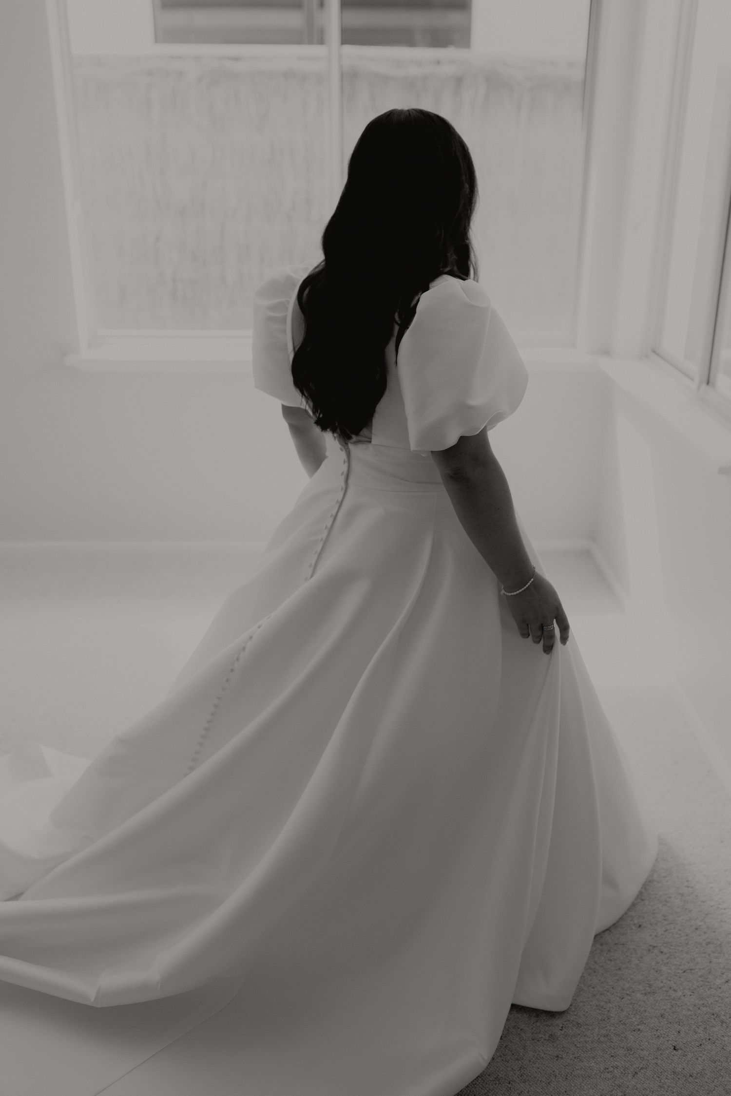 Bride in elegant white puff sleeve wedding gown with long train viewed from behind in black and white.