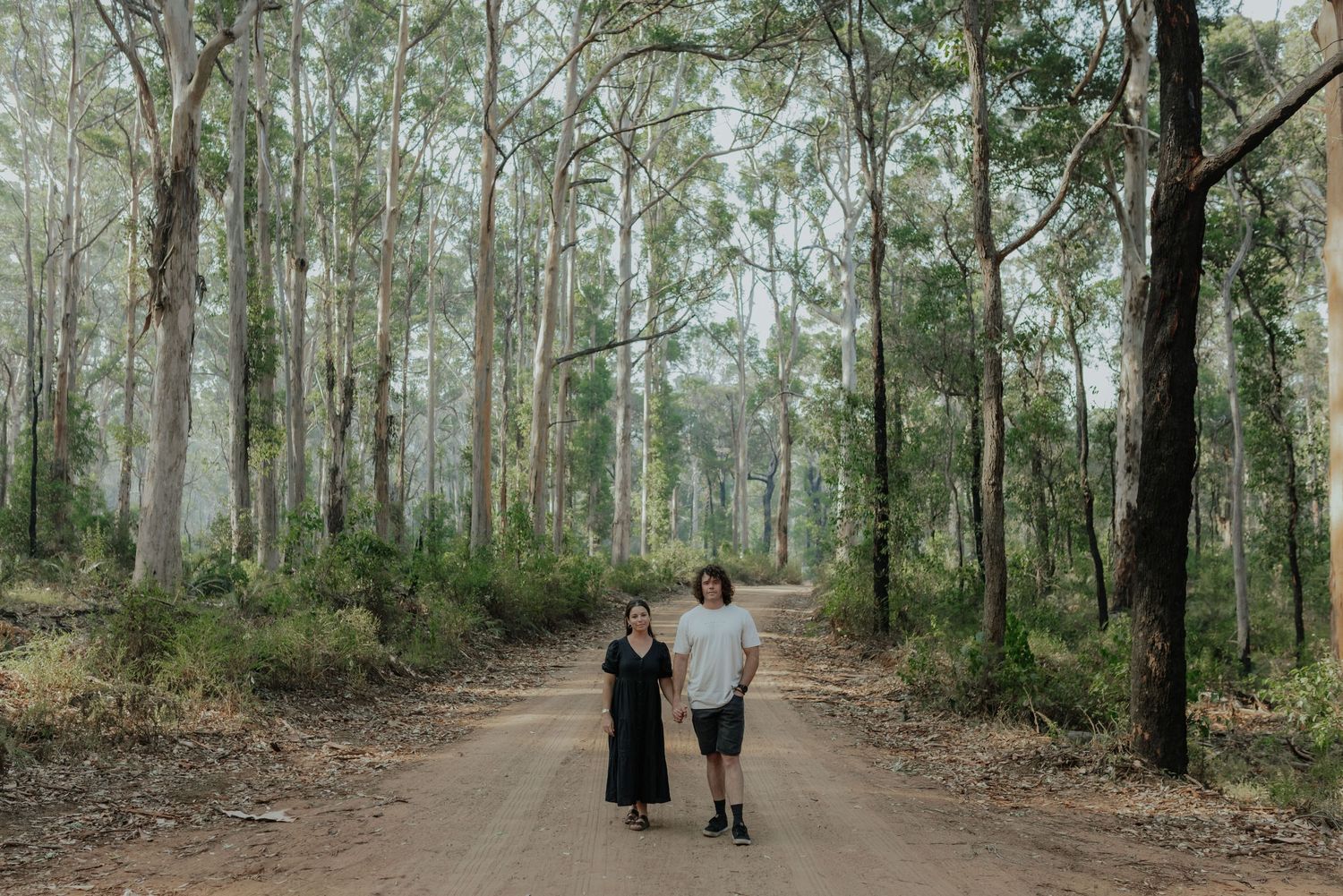 Couple walking hand in hand down a scenic dirt road surrounded by tall eucalyptus trees.