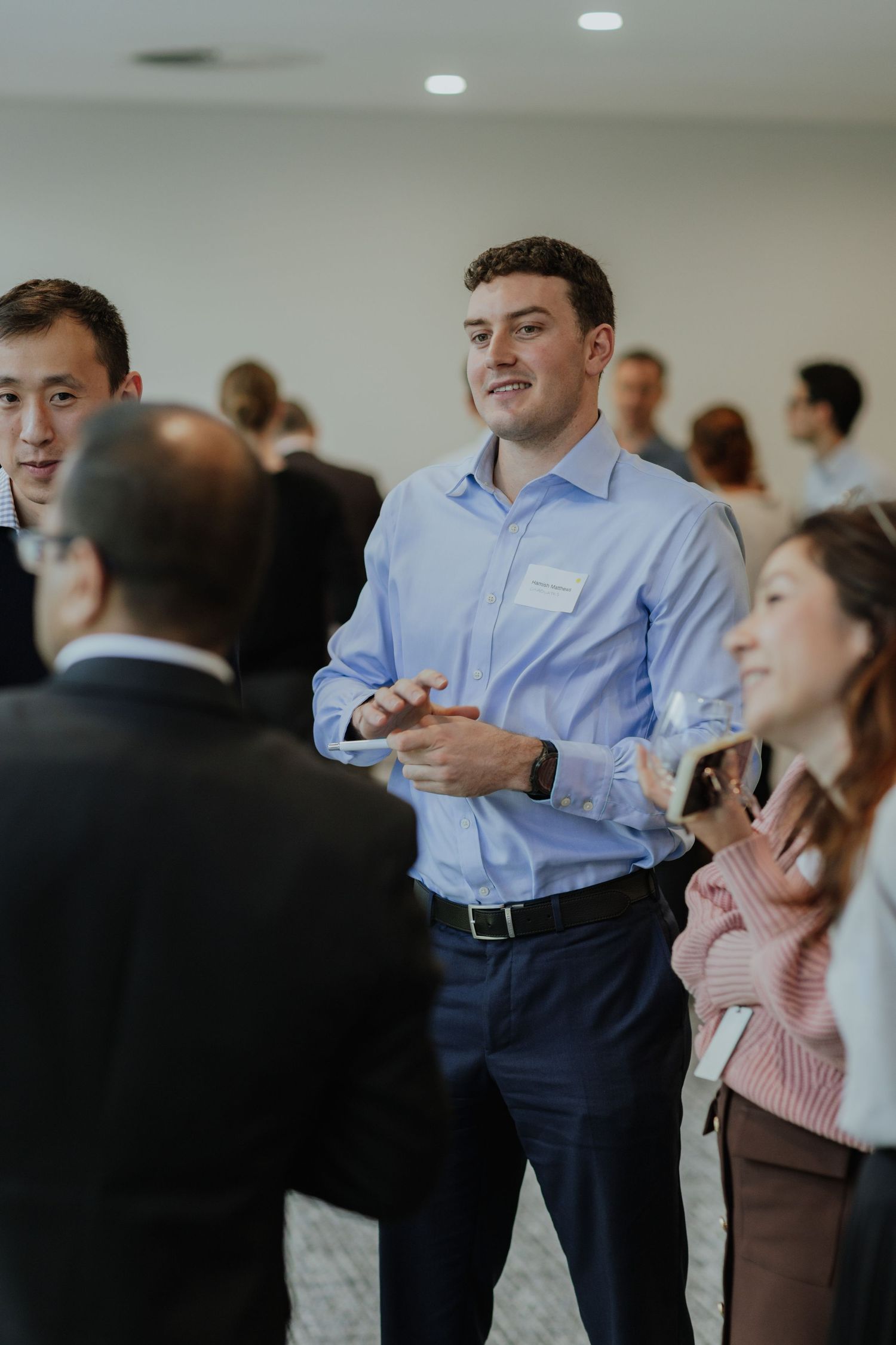 Young professional man in blue shirt networking and conversing with colleagues at a corporate business event.
