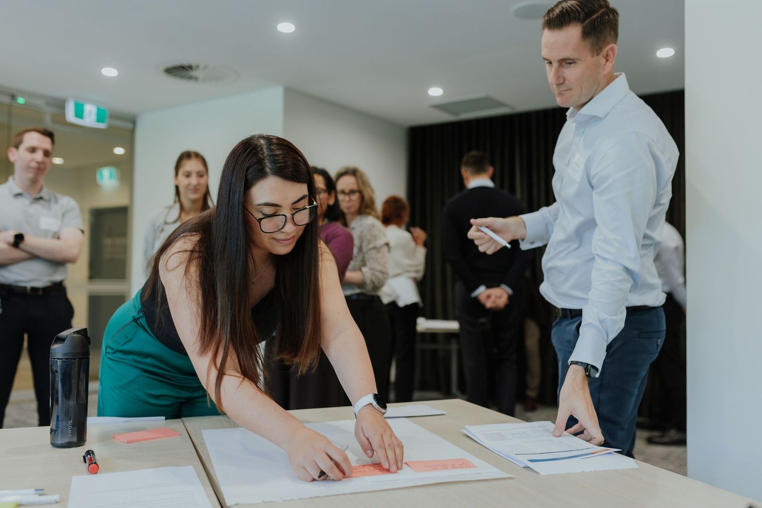 Professional woman in green dress reviews documents at a table during a business workshop.