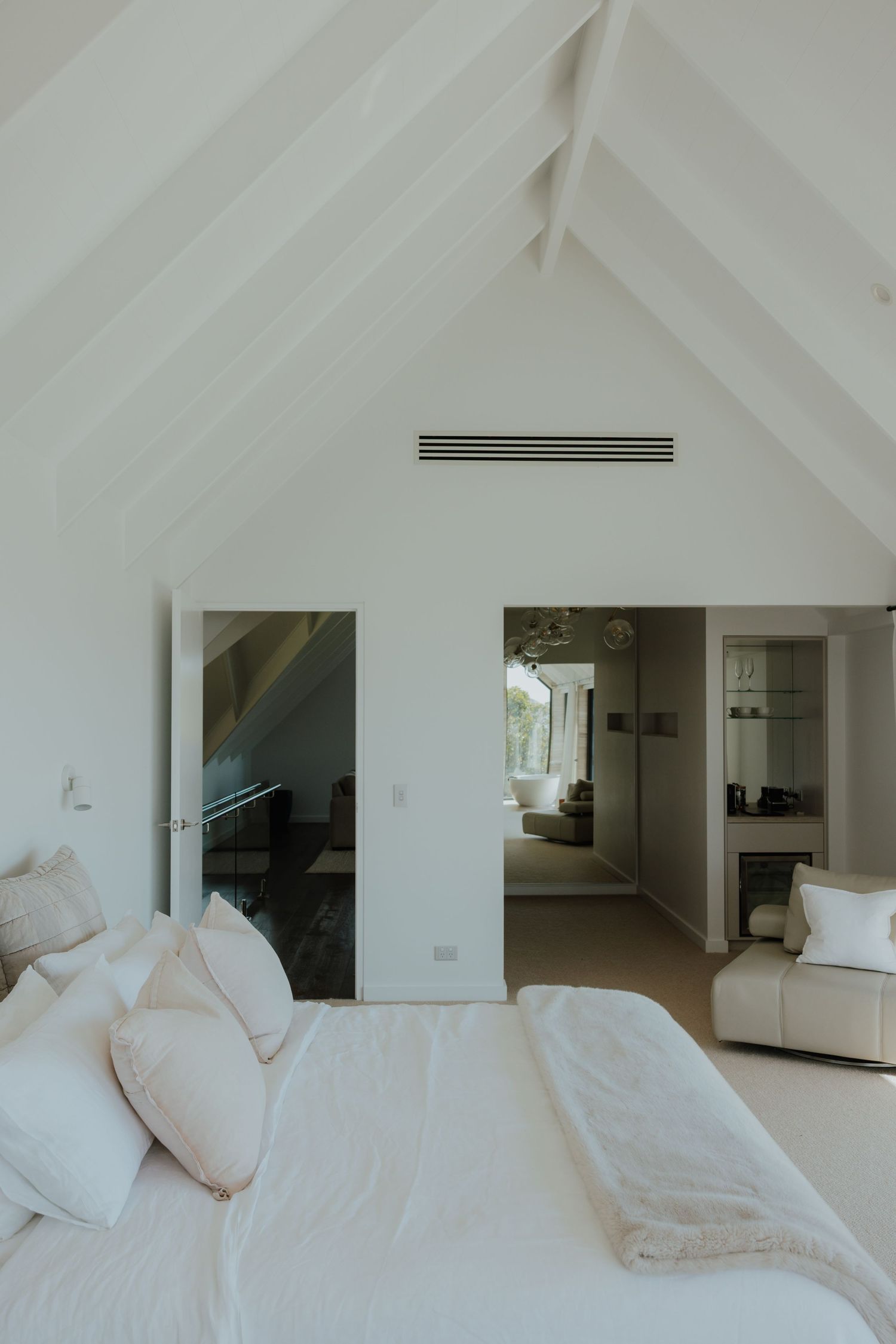 Bright white bedroom with vaulted ceiling and open doorways leading to adjoining rooms.