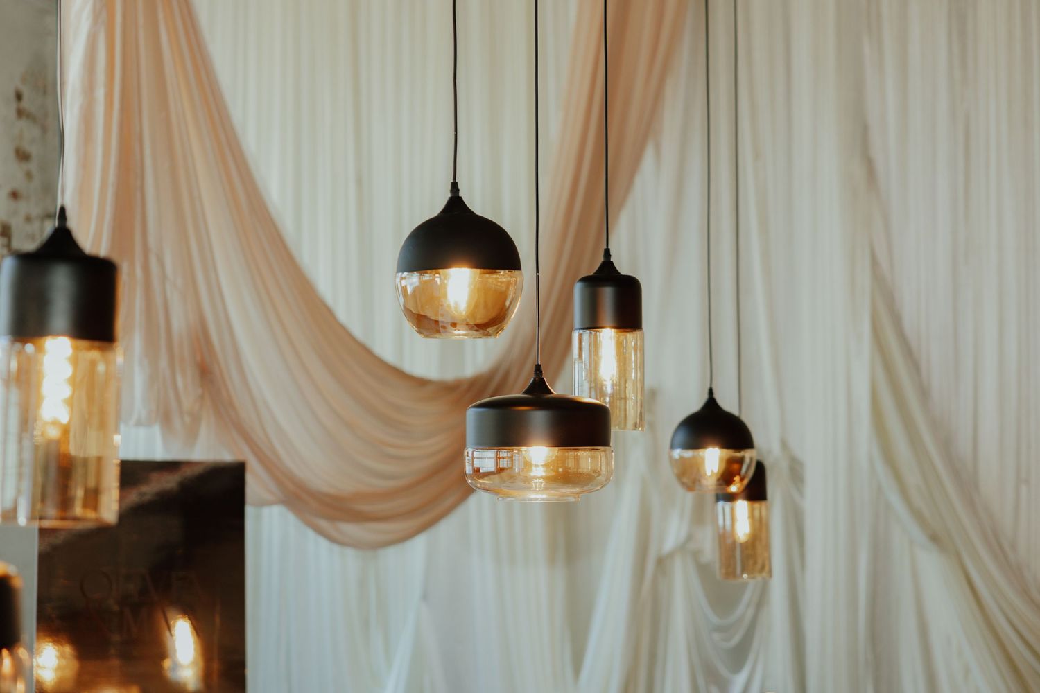 Cluster of black and amber glass pendant lights hanging against draped cream fabric wedding backdrop.