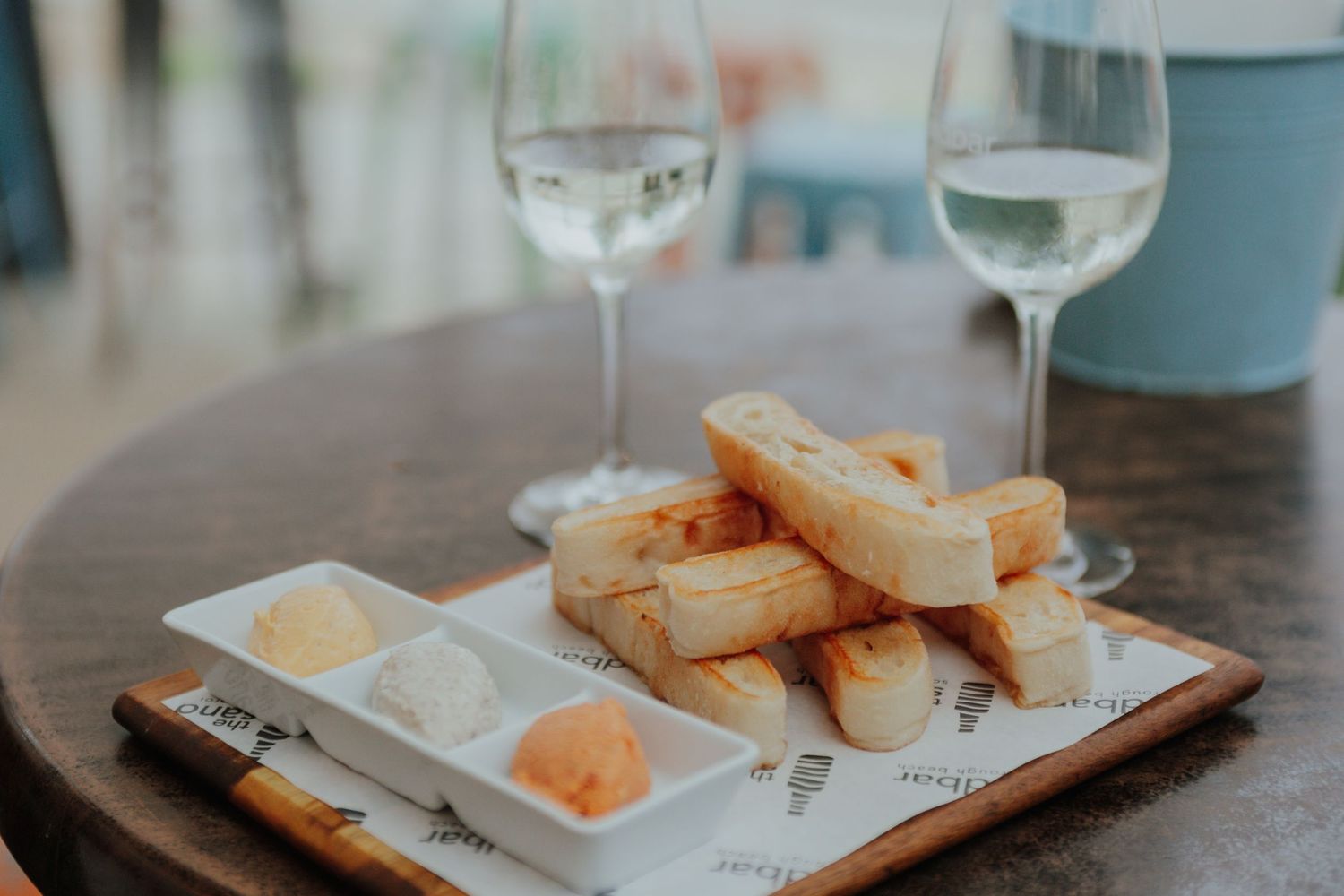 Toasted bread sticks served with dipping sauces alongside two glasses of white wine.