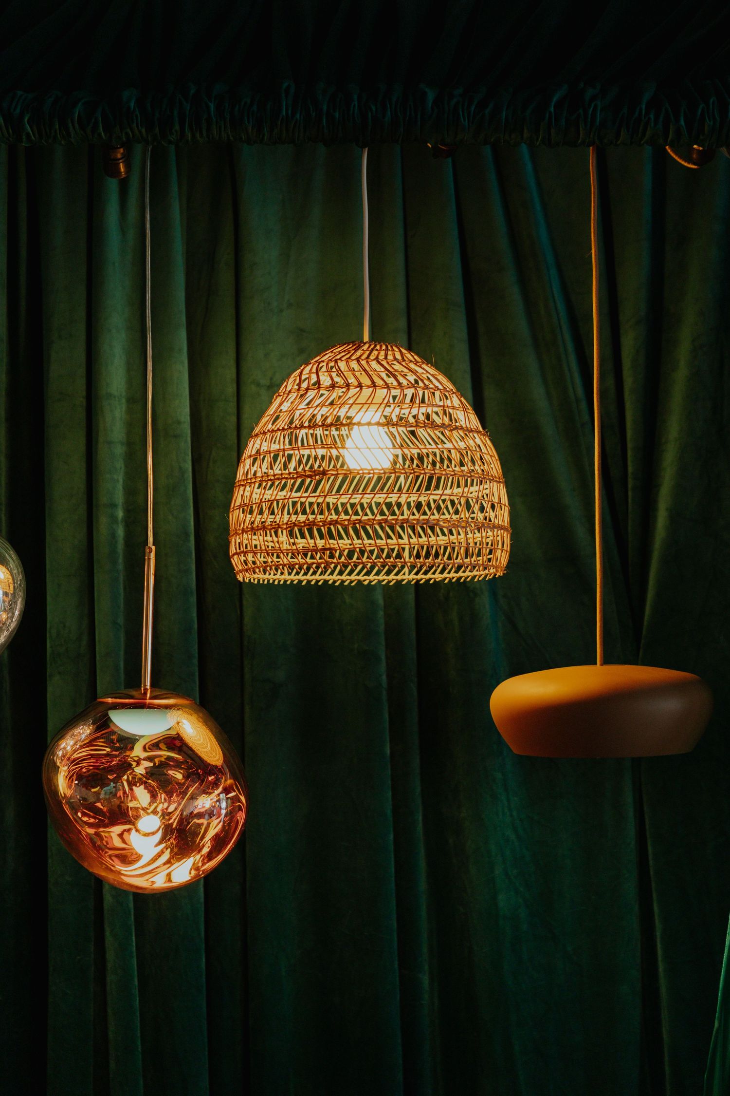 Warm wicker dome pendant light with copper globe and mustard disc lamp against green velvet backdrop.