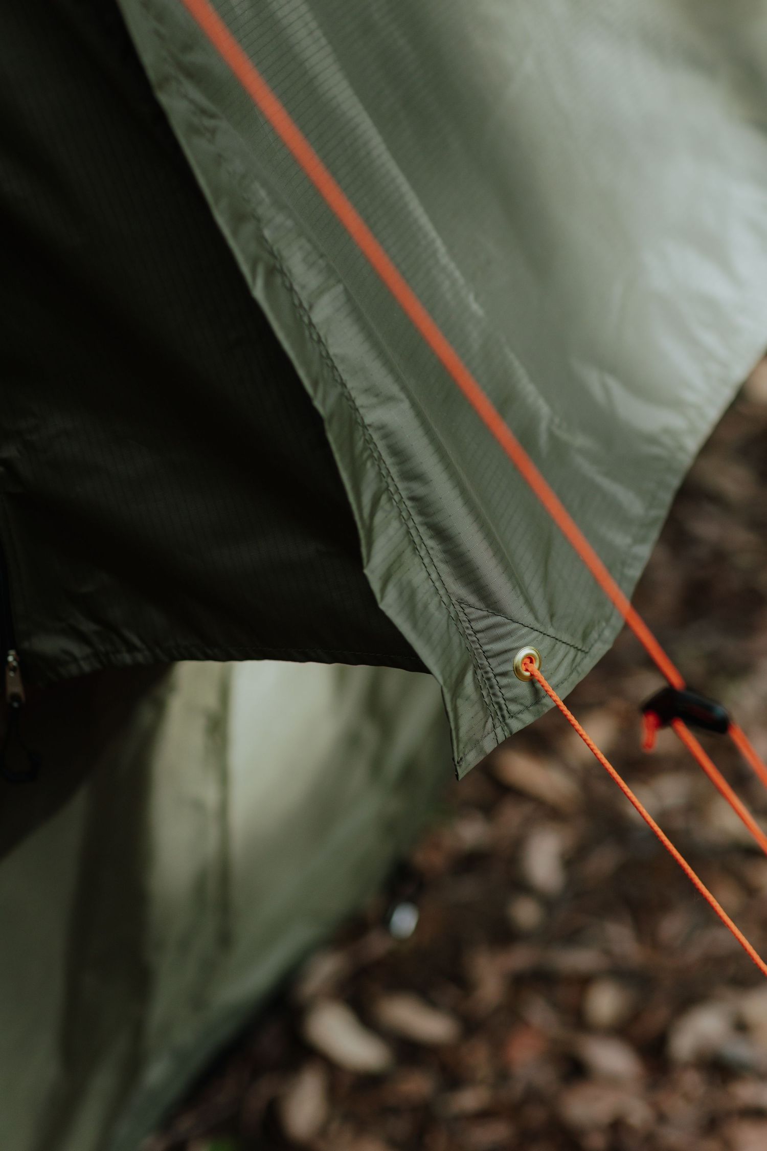 Close-up detail of olive green camping tent with orange guy ropes in an outdoor setting.