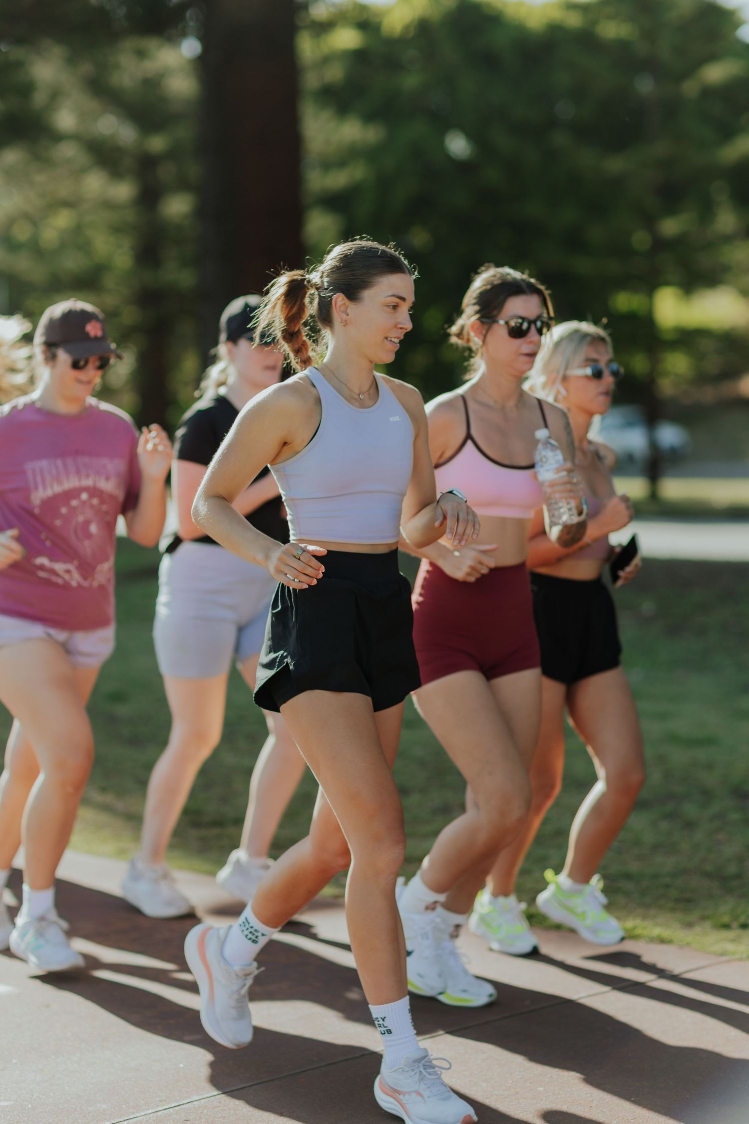 Group of women in colorful activewear jogging together along a sunlit park pathway.