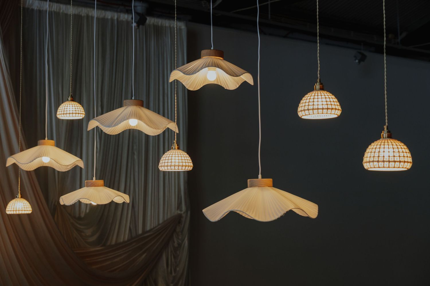 Collection of unique pendant lights including wavy white shades and wicker dome styles hanging against draped curtains.