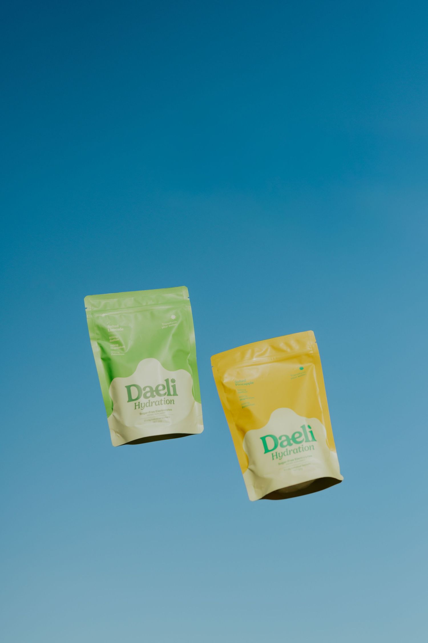 Two Daeli Hydration pouches in green and yellow floating against a clear blue sky.