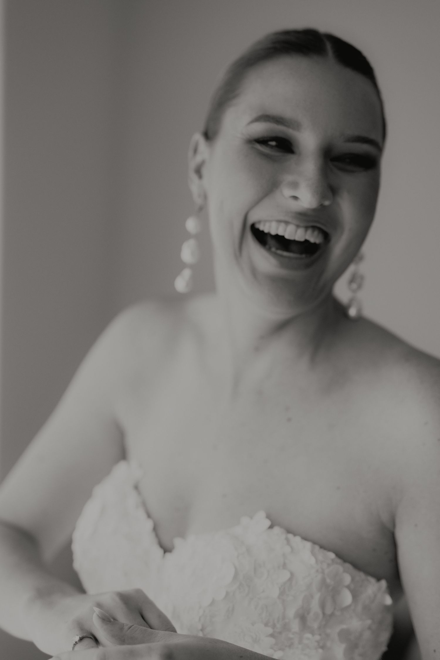 Joyful bride in strapless lace wedding dress laughing candidly in black and white portrait.
