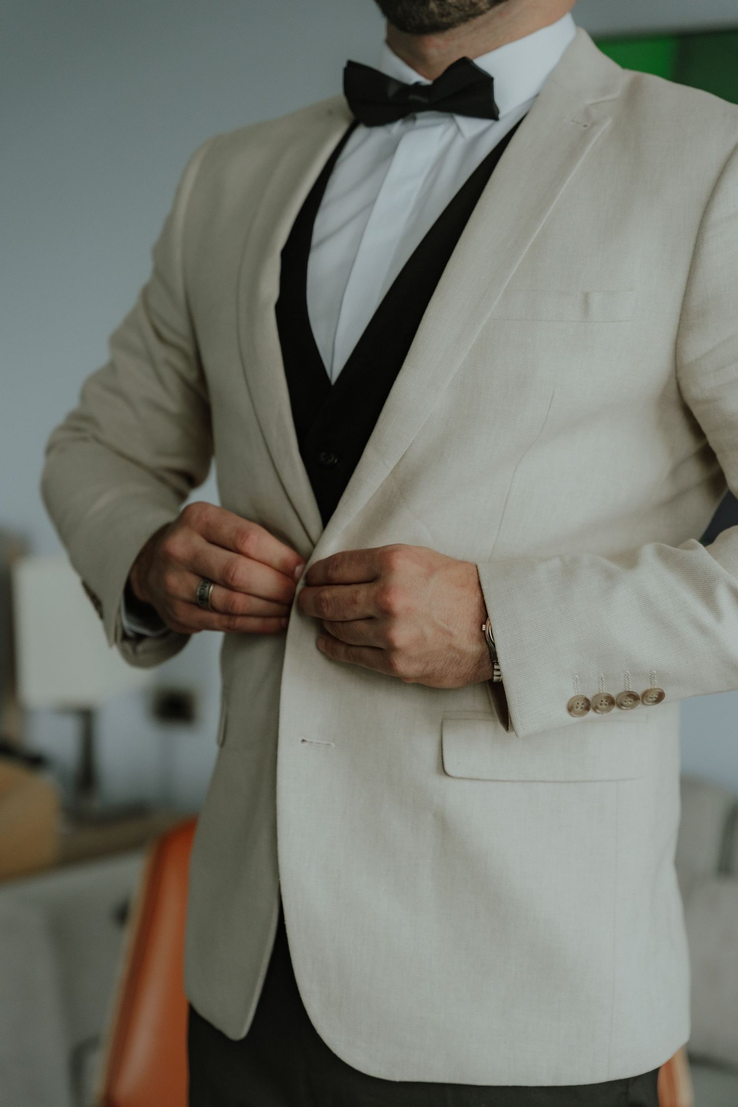 Groom in cream tuxedo jacket with black lapels and bow tie buttoning his jacket before the wedding.