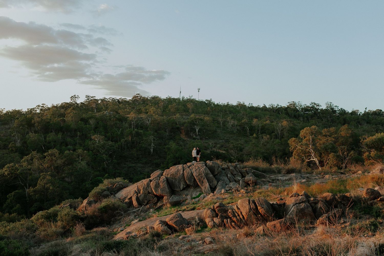 Distant view of a person standing on rocky terrain with a scenic Australian bush landscape.