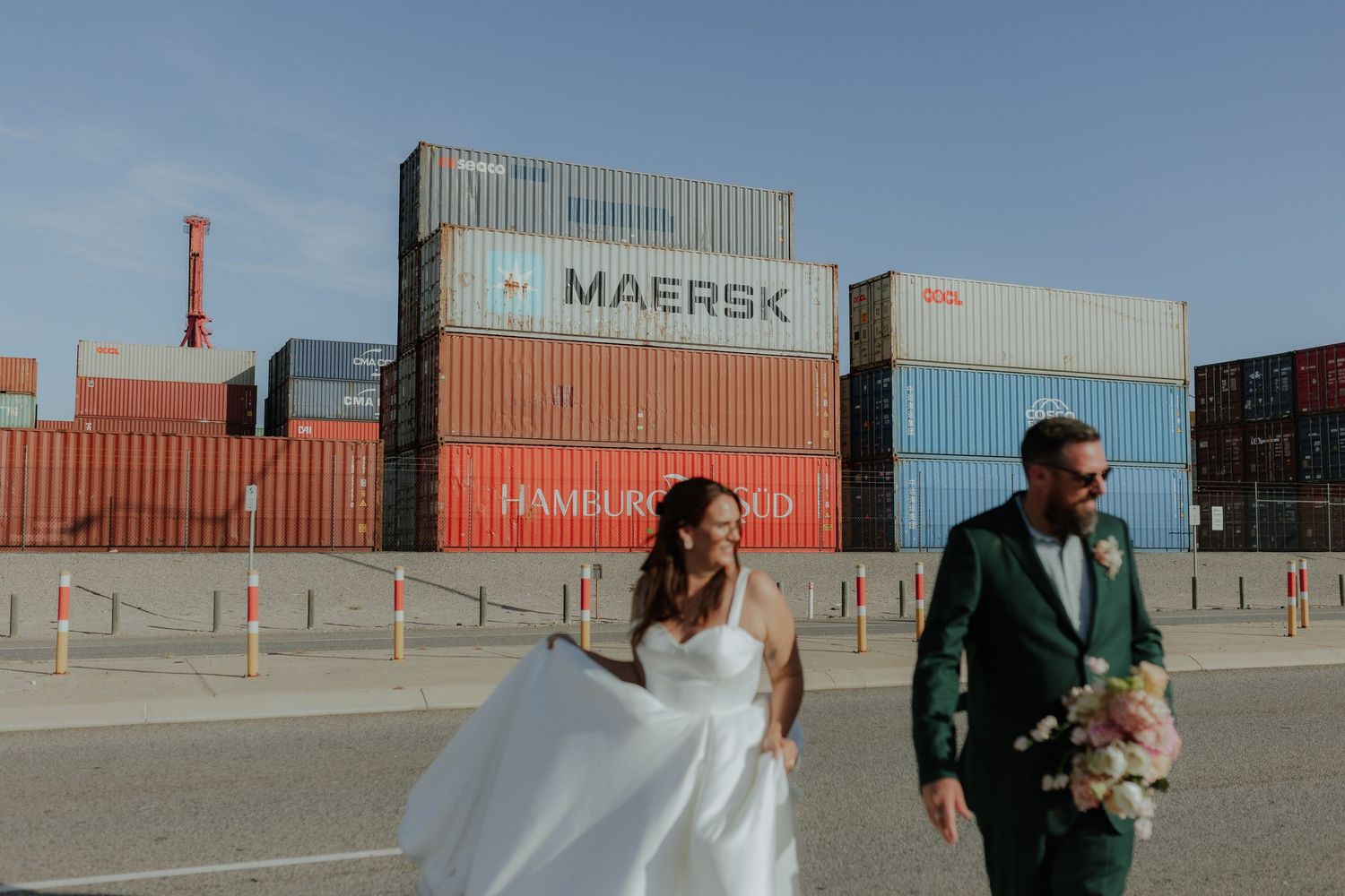 Bride and groom walking past colorful Maersk shipping containers at industrial port wedding photo location.