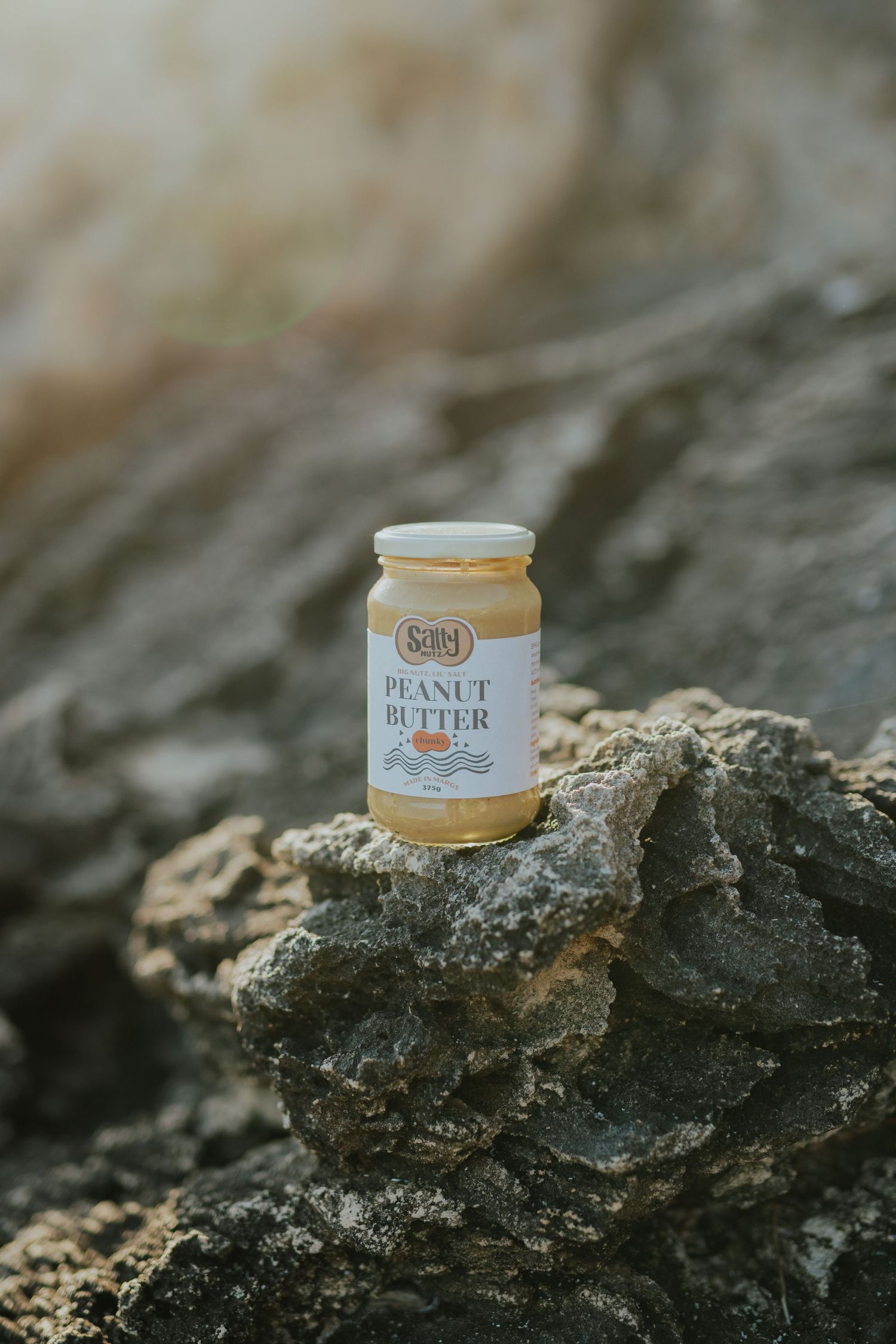 Jar of Seitels peanut butter sitting on rugged rocks outdoors in natural sunlight.