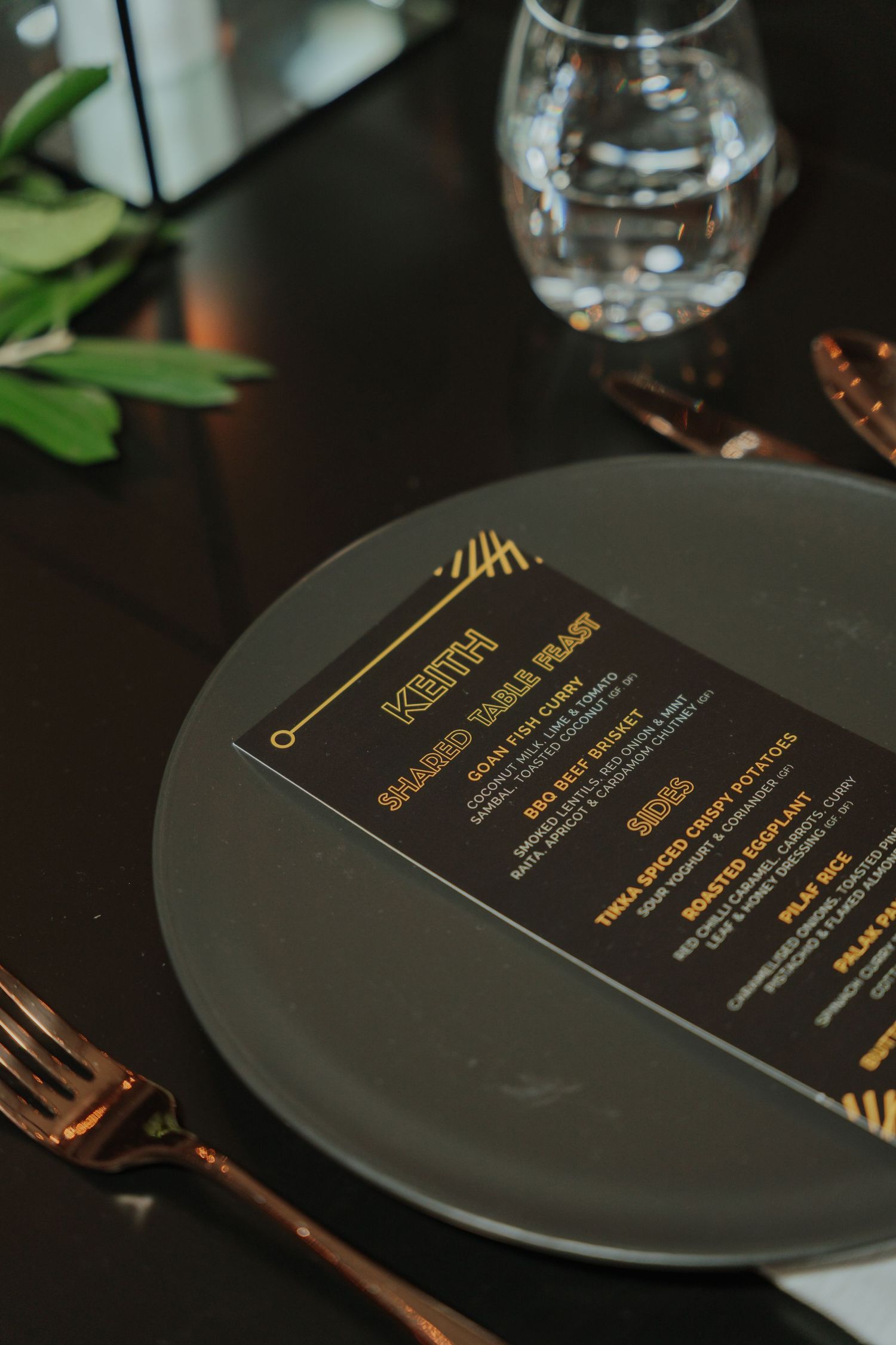 Black plate with gold-printed personalized menu card and copper cutlery at a formal dinner.