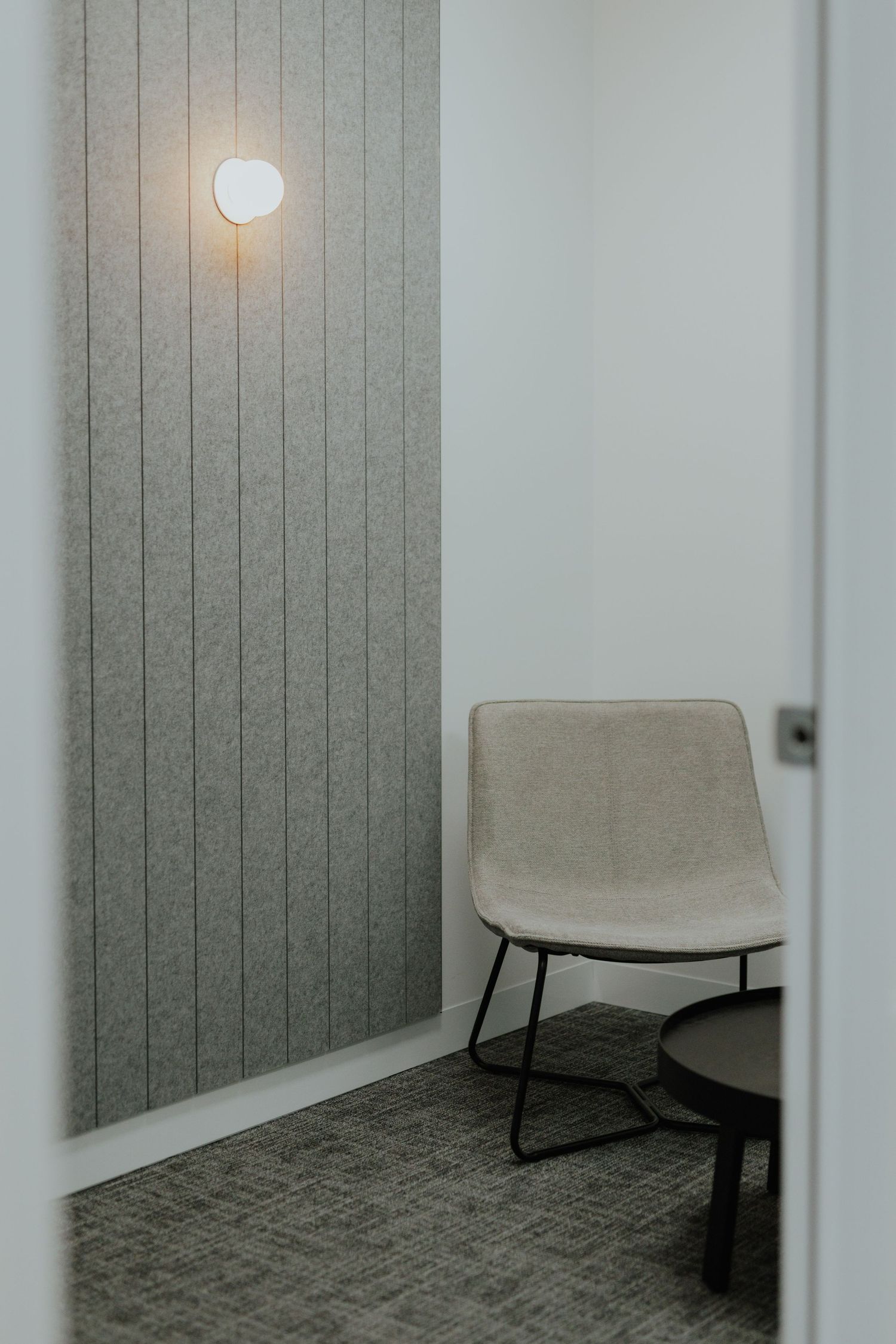 Cozy private office nook with beige lounge chair, round table, and warm wall sconce light.