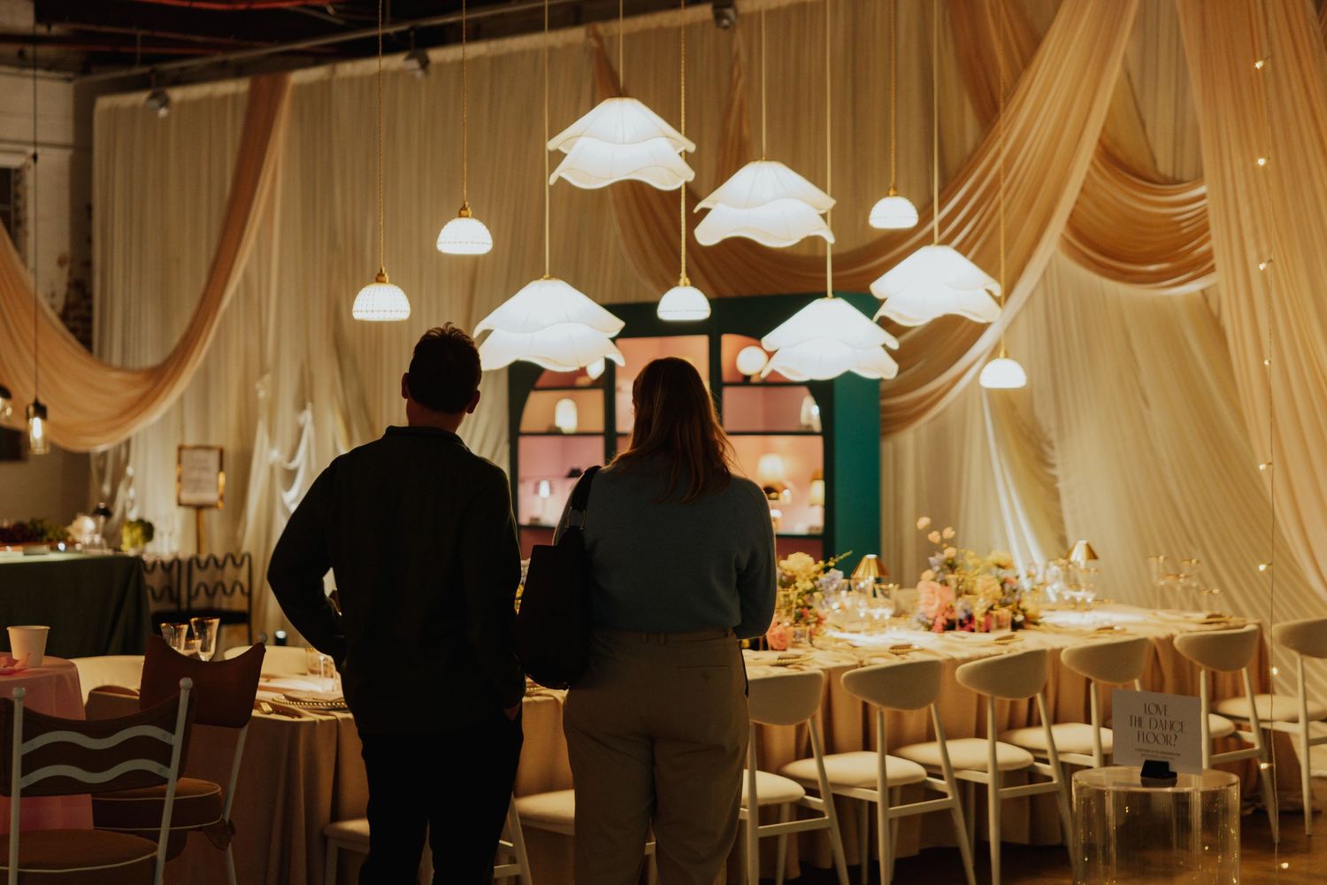 Two silhouetted guests admire a long decorated banquet table with cloud-shaped pendant lights.