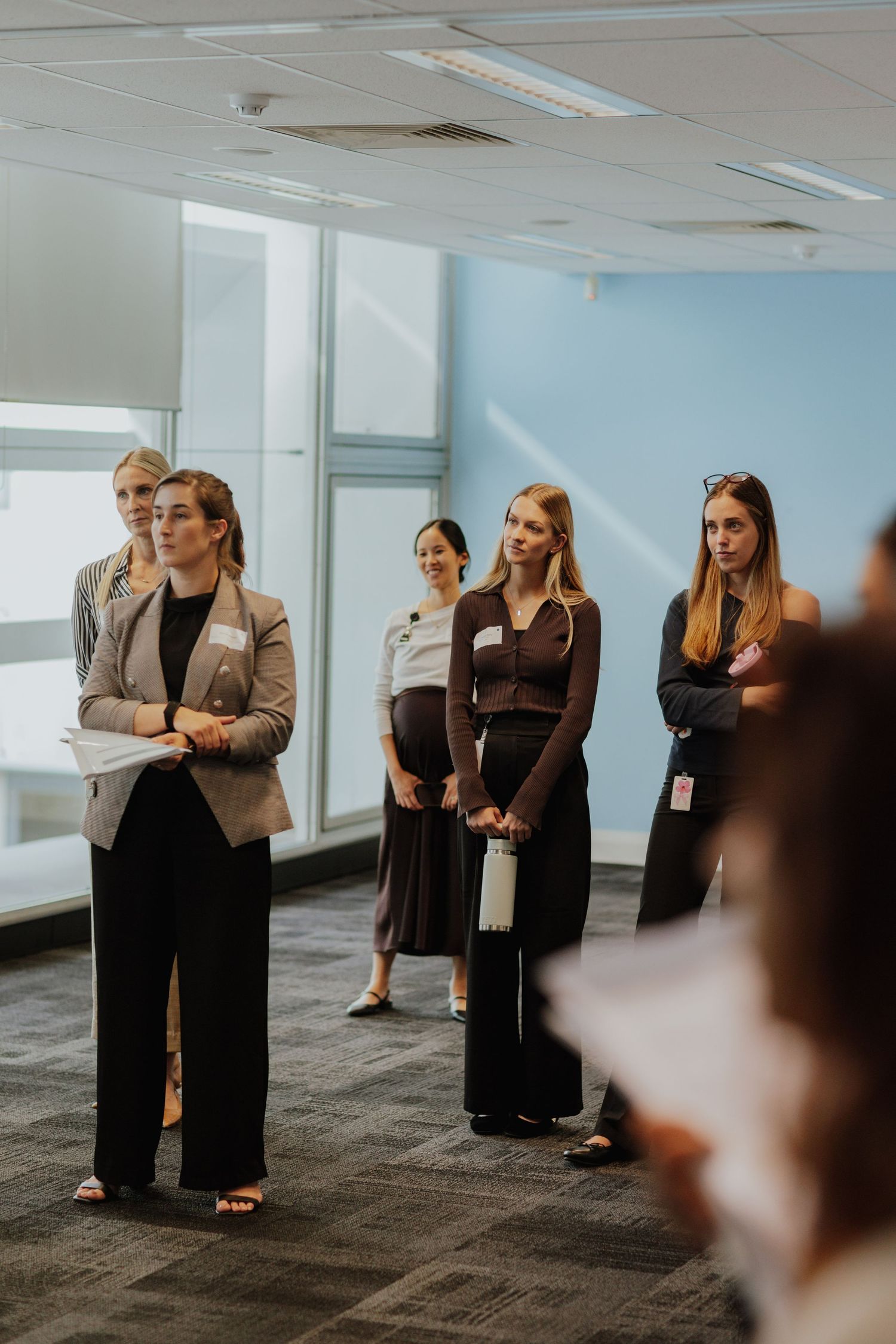 Group of professional women in business attire listening attentively at a corporate workshop.
