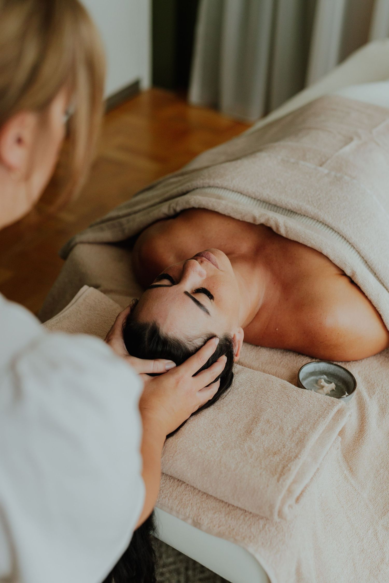 Massage therapist performing a relaxing head massage on a client lying on a treatment table.