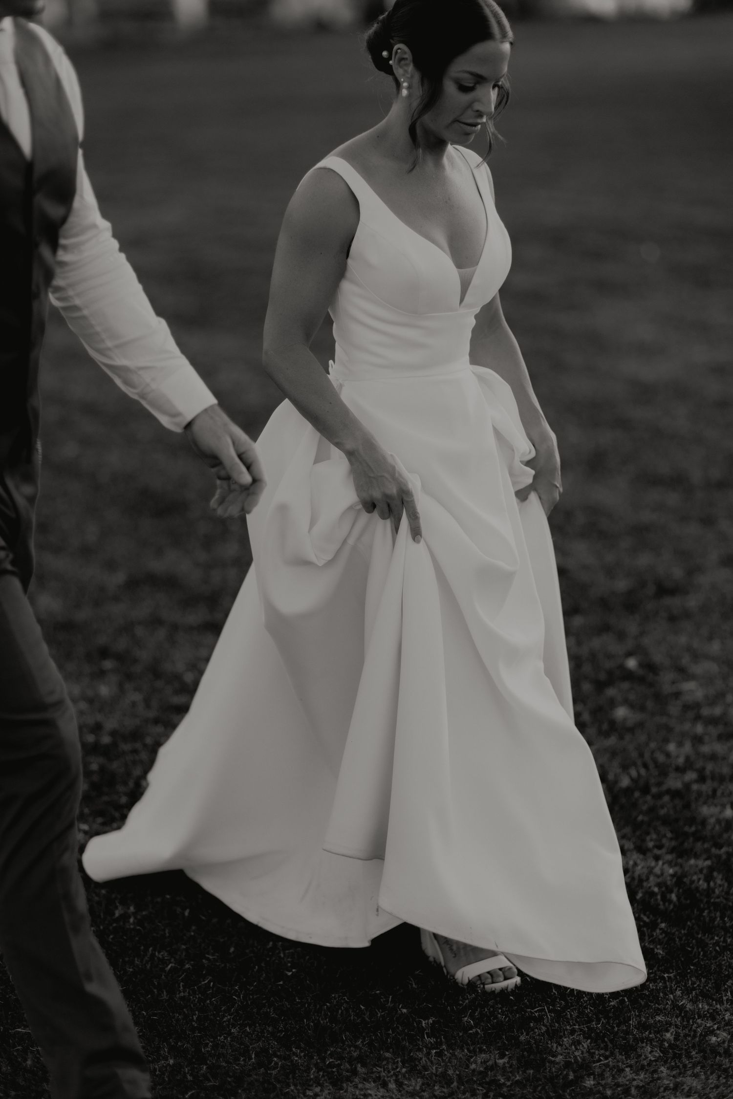 Bride in elegant A-line wedding gown walks gracefully outdoors in black and white photo.