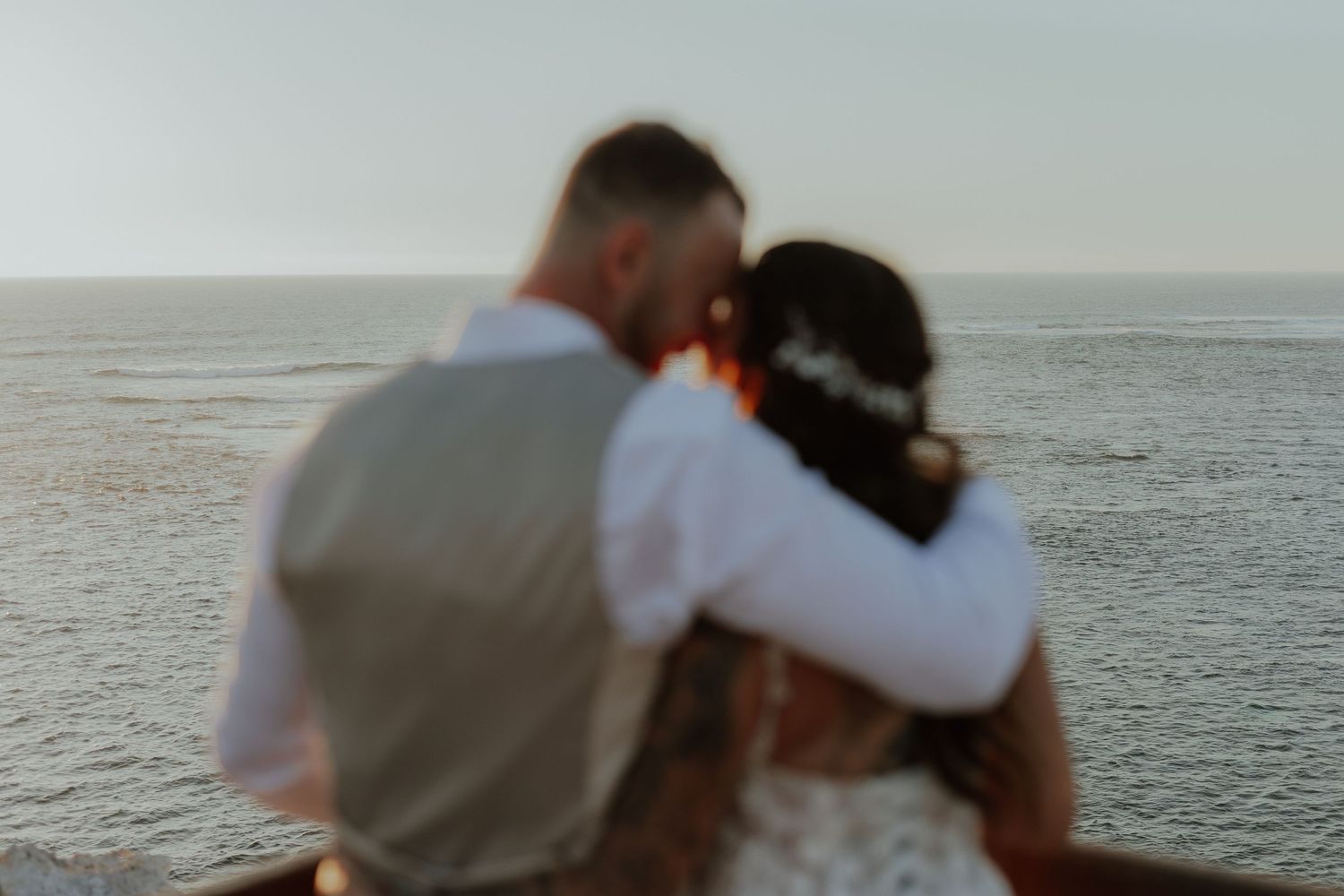Bride and groom embracing while overlooking the ocean at golden hour during their wedding.