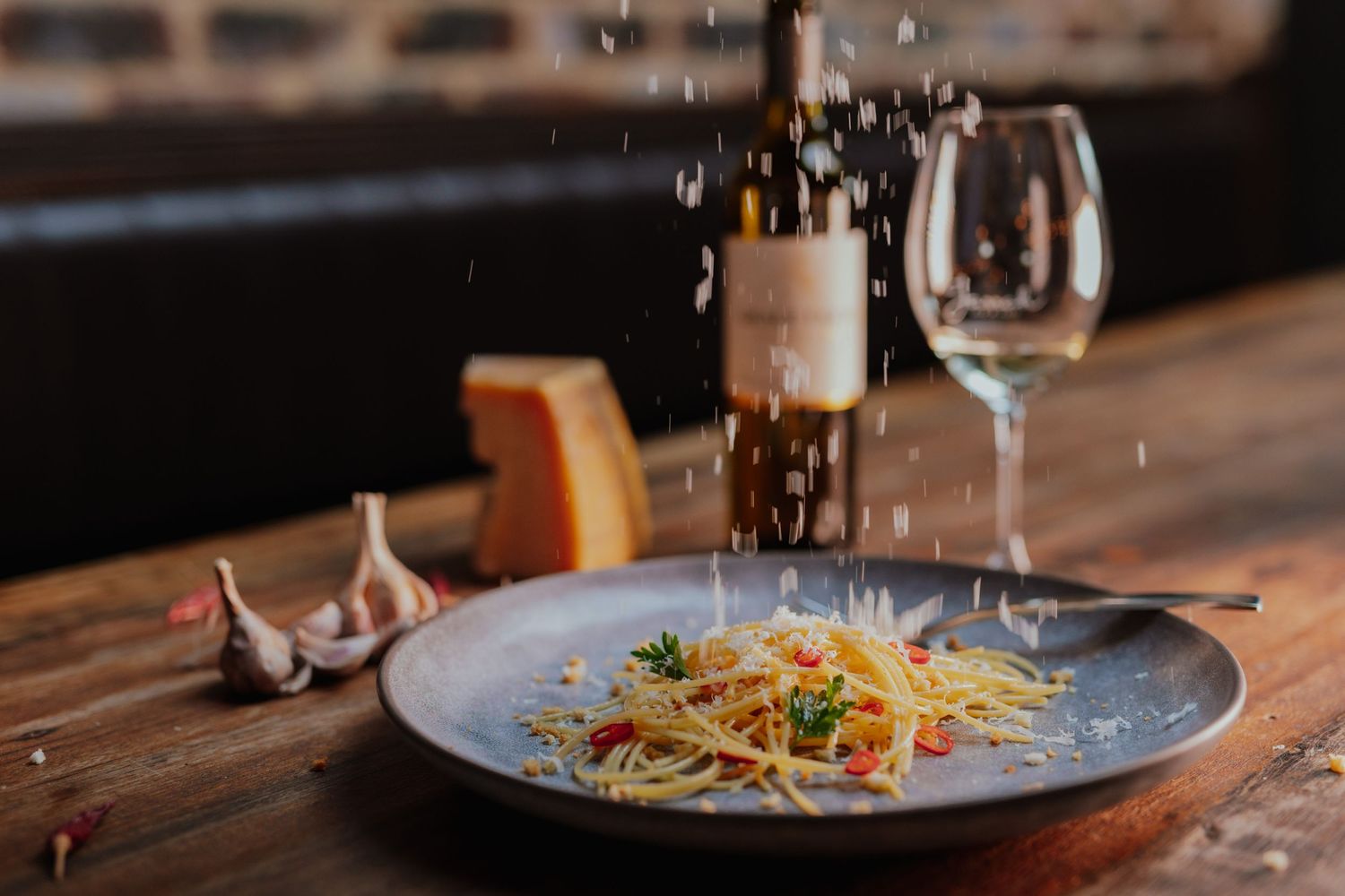Plate of spaghetti aglio e olio with parmesan being grated over it, served with white wine.