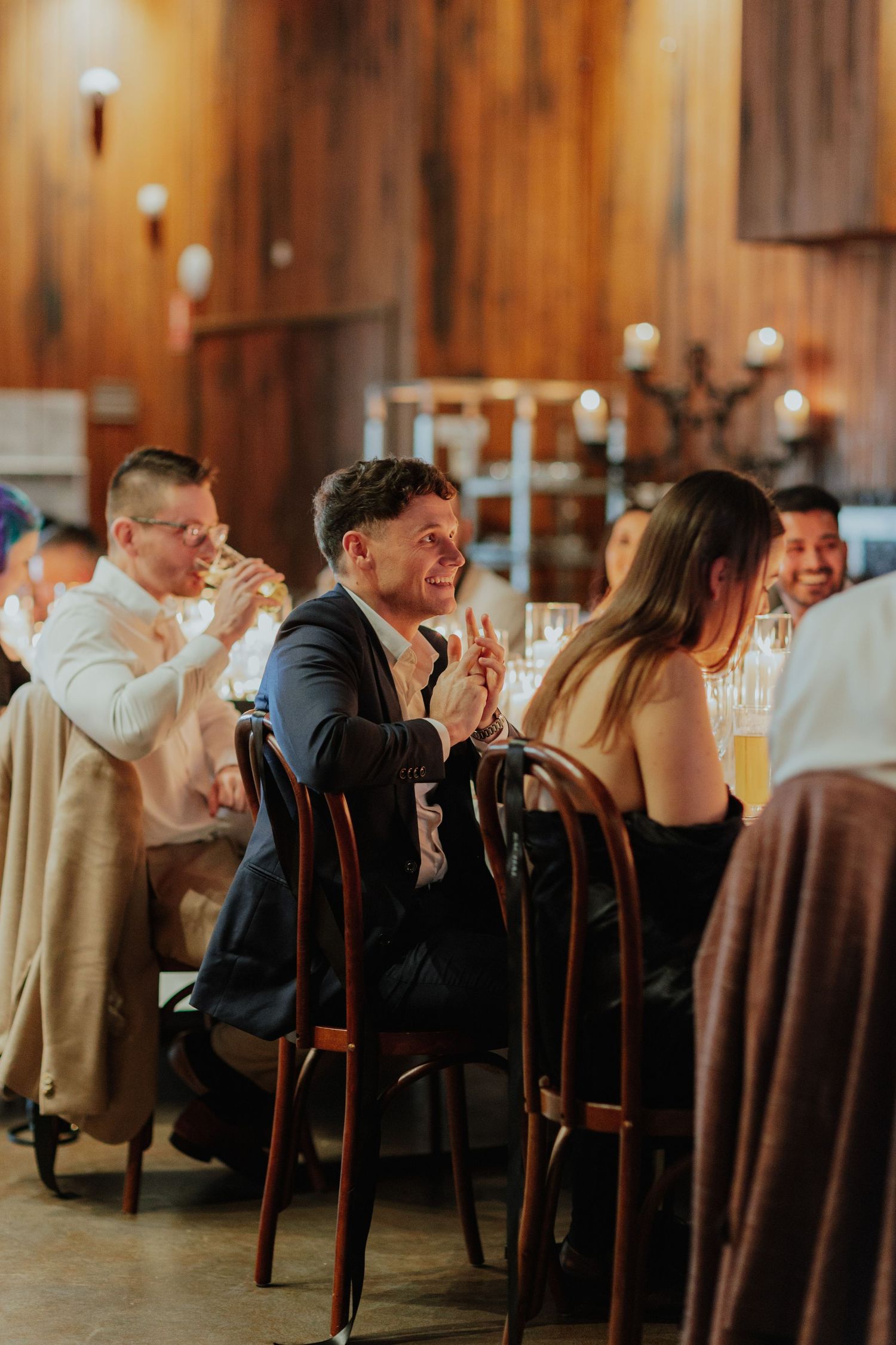 Guests laughing and clapping at a formal dinner event in a warmly lit winery venue.