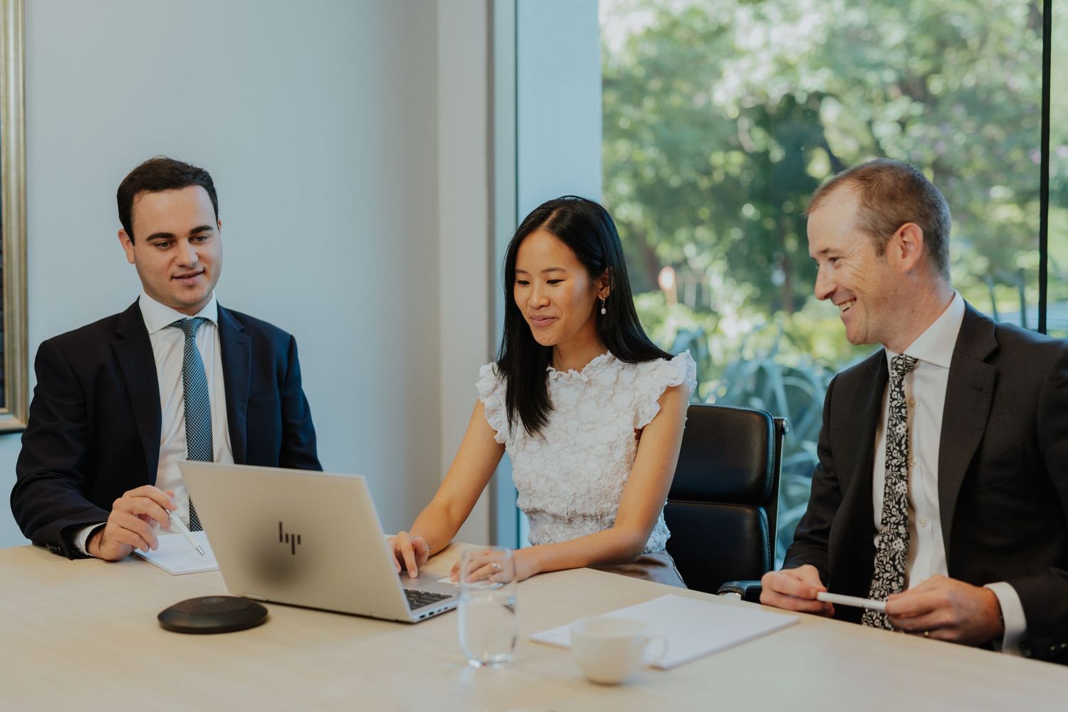 Three business professionals collaborating on HP laptop during corporate meeting in bright office.