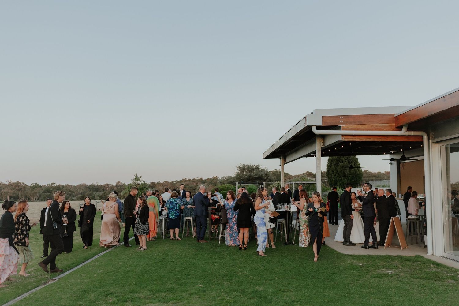 Wedding guests mingling on green lawn outside venue at dusk during outdoor reception.