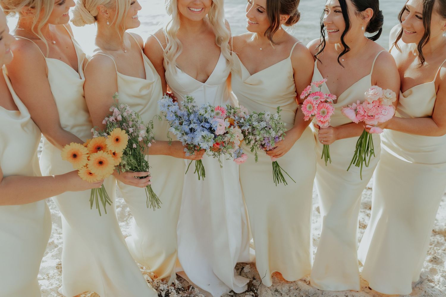 Bride and bridesmaids in cream dresses holding colorful spring wedding bouquets.