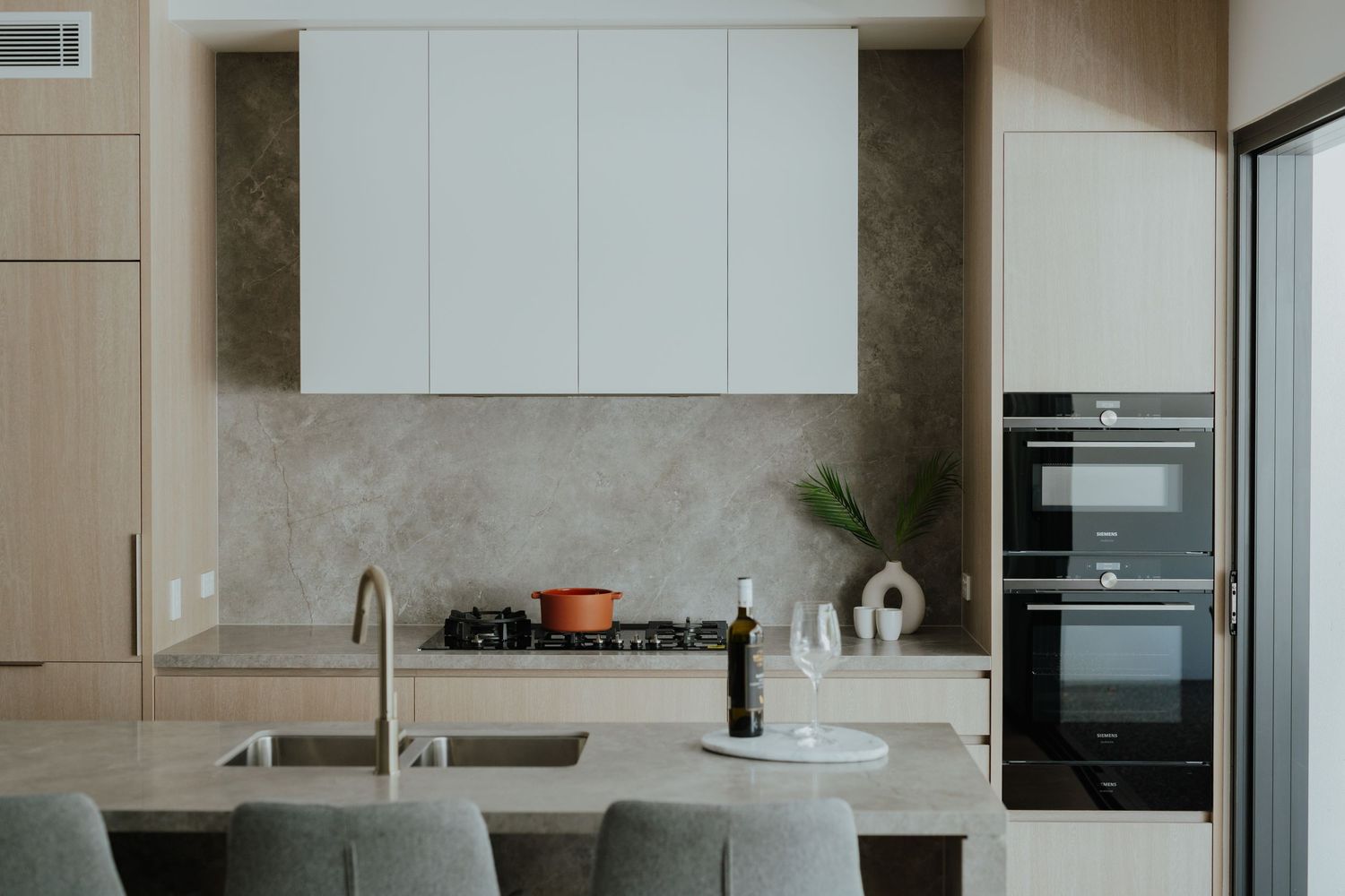 Contemporary kitchen featuring white cabinetry, stone benchtop, gas cooktop, double ovens, and island bar.