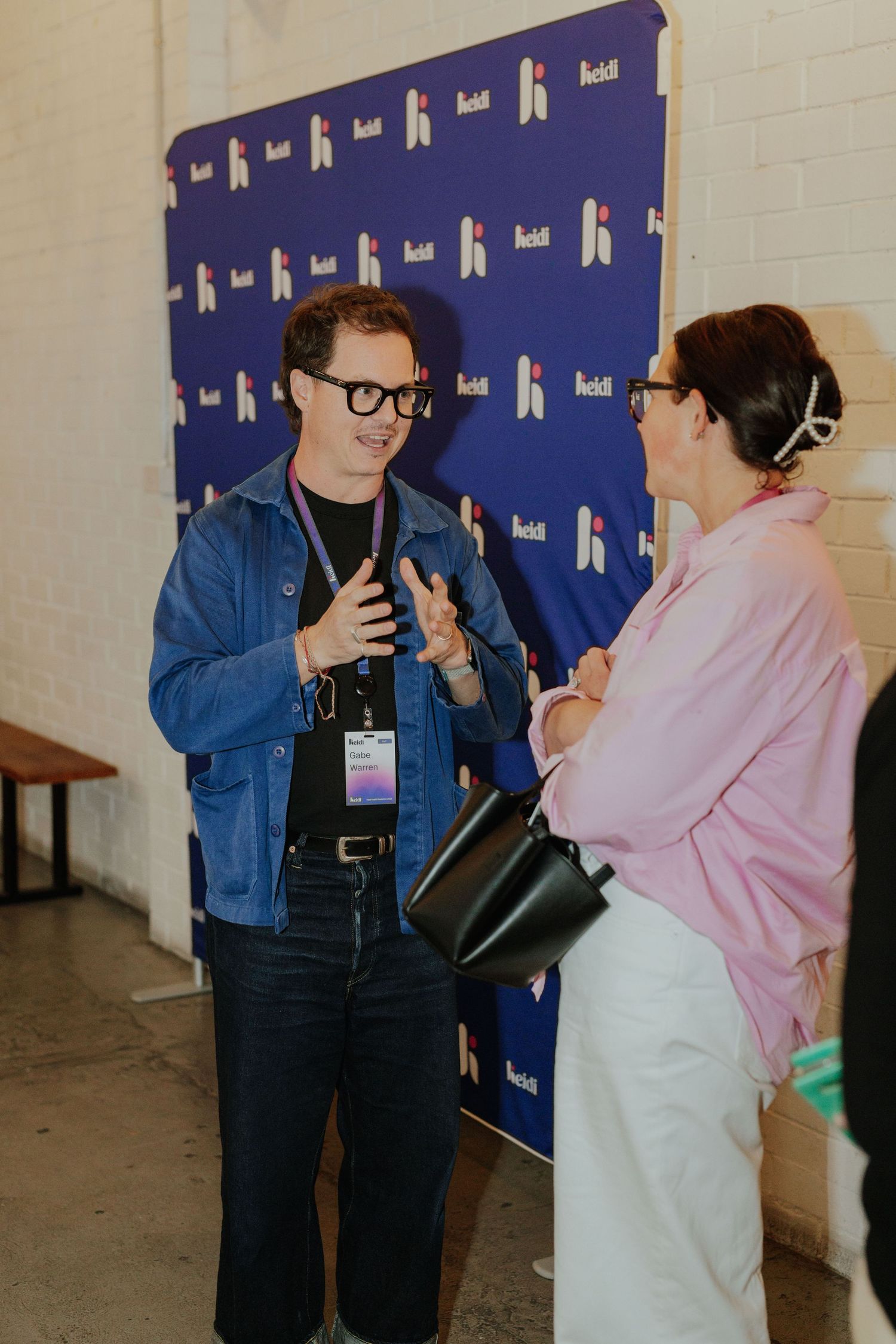 Two people networking and conversing in front of a branded blue event backdrop at a conference.