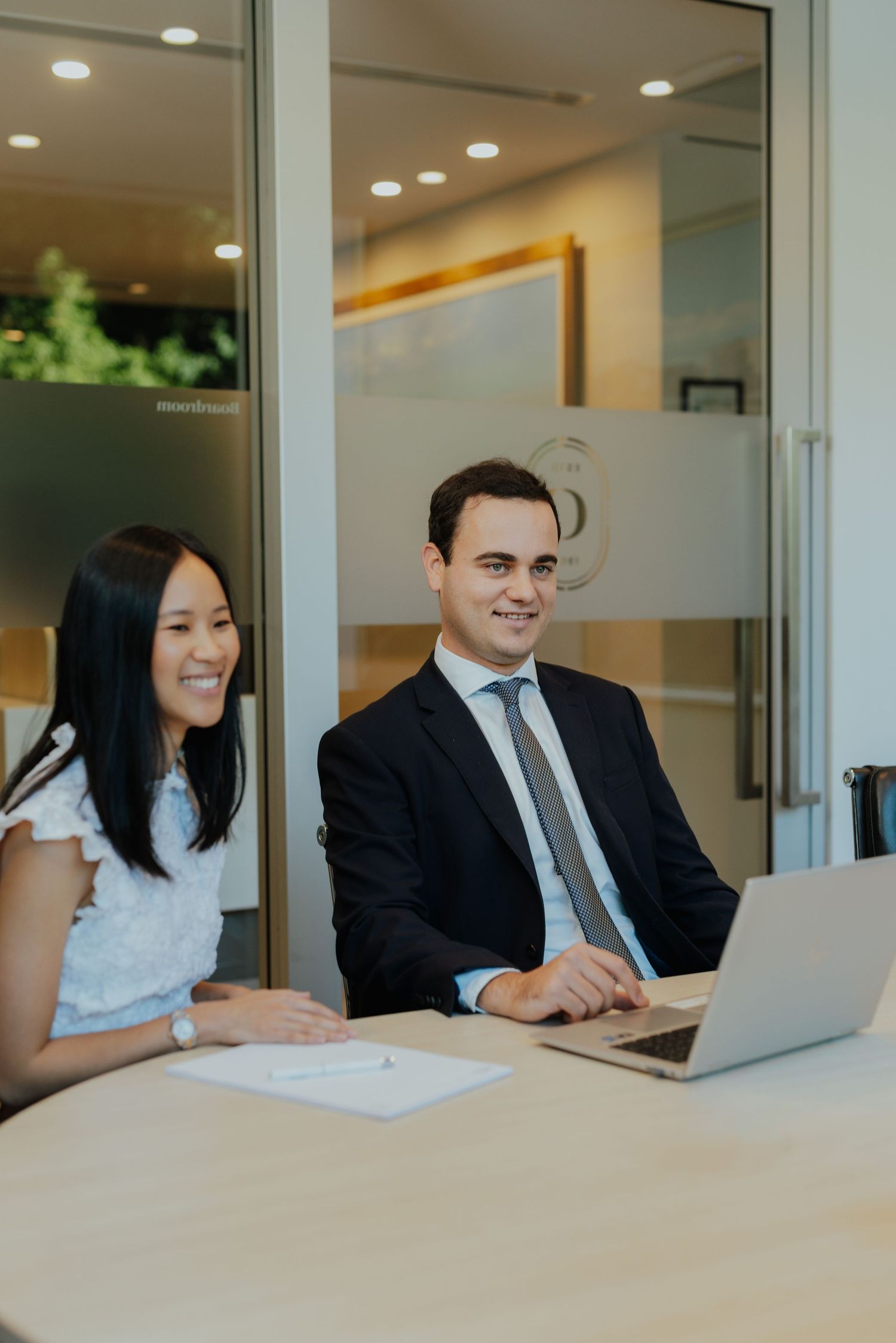 Two business professionals smiling and collaborating on laptop computer during office meeting.