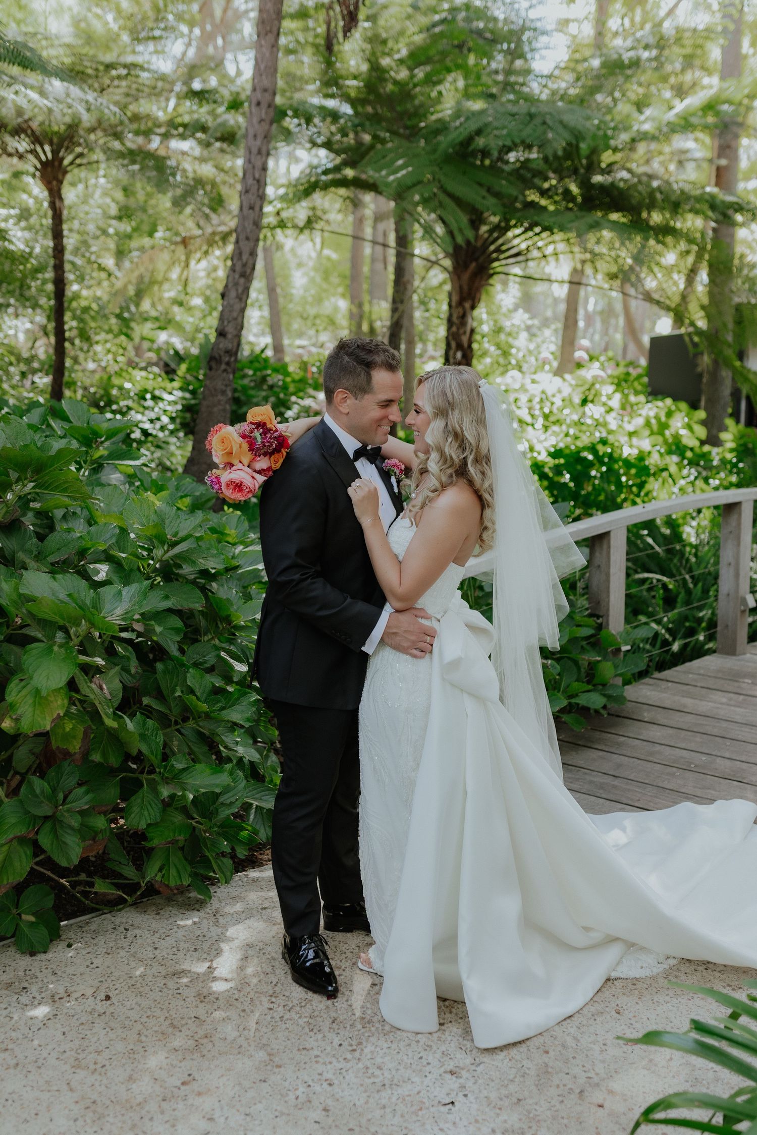 Bride and groom sharing a tender moment surrounded by lush green tropical garden on wooden walkway.
