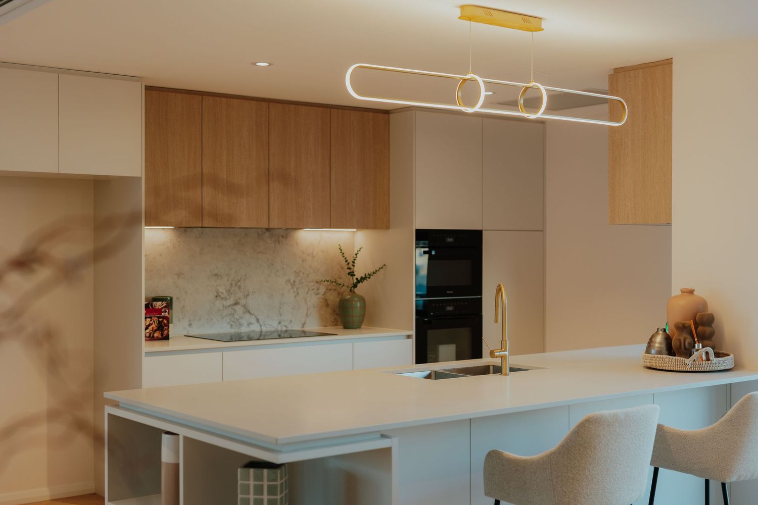 Contemporary kitchen with timber and white cabinetry, marble splashback, white island bench, and gold pendant light.