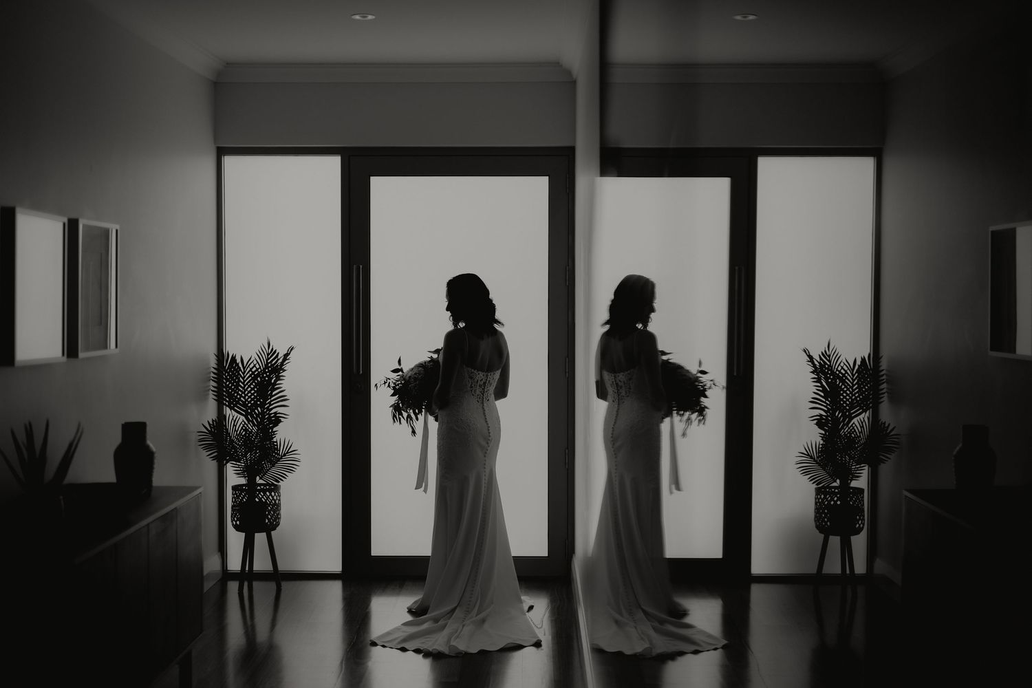 Black and white mirror reflection of bride holding bouquet by doors.