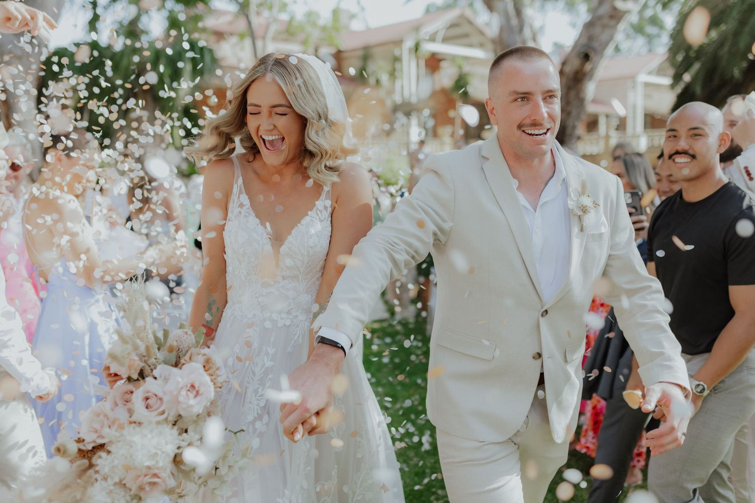 Joyful bride and groom walking through confetti shower at outdoor wedding ceremony.