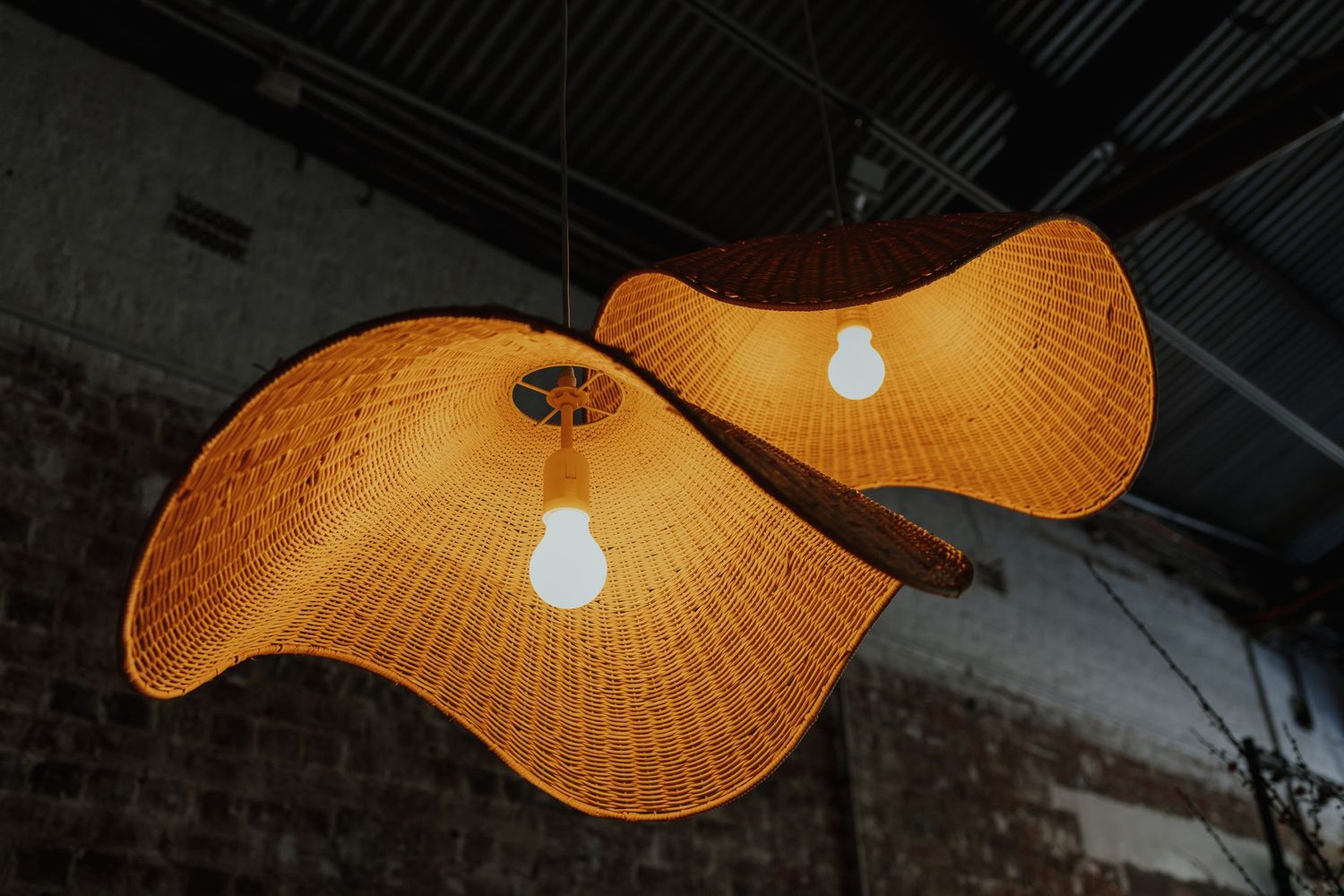 Two illuminated woven rattan pendant lights glowing warmly against a dark brick ceiling.