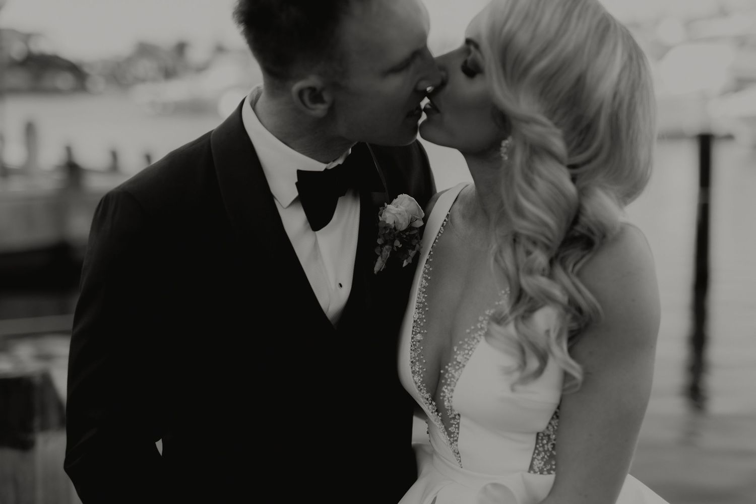 Black and white photo of a bride and groom sharing a romantic kiss at their waterfront wedding.