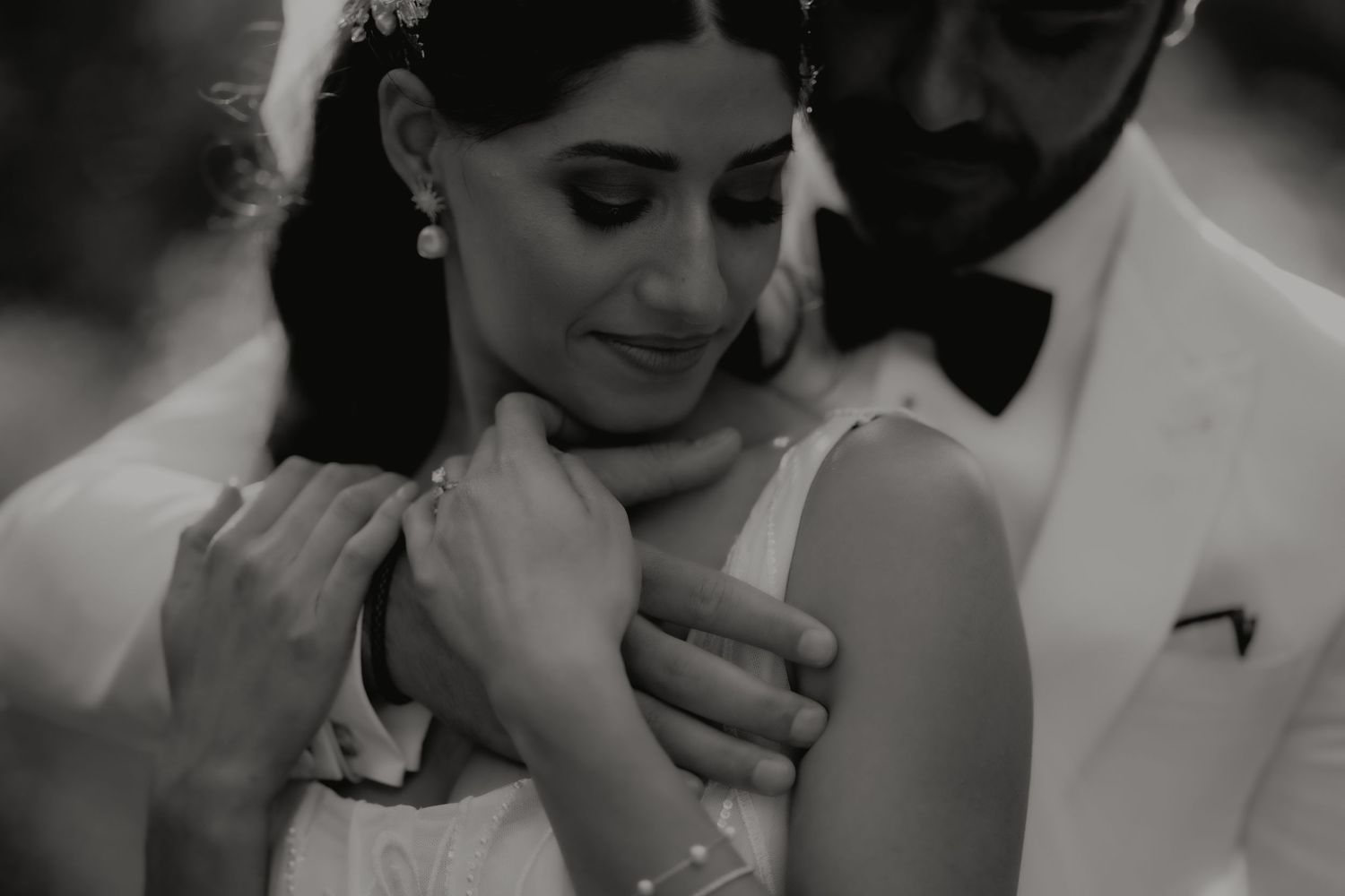Intimate black and white close-up of groom in white suit tenderly holding brides shoulders.