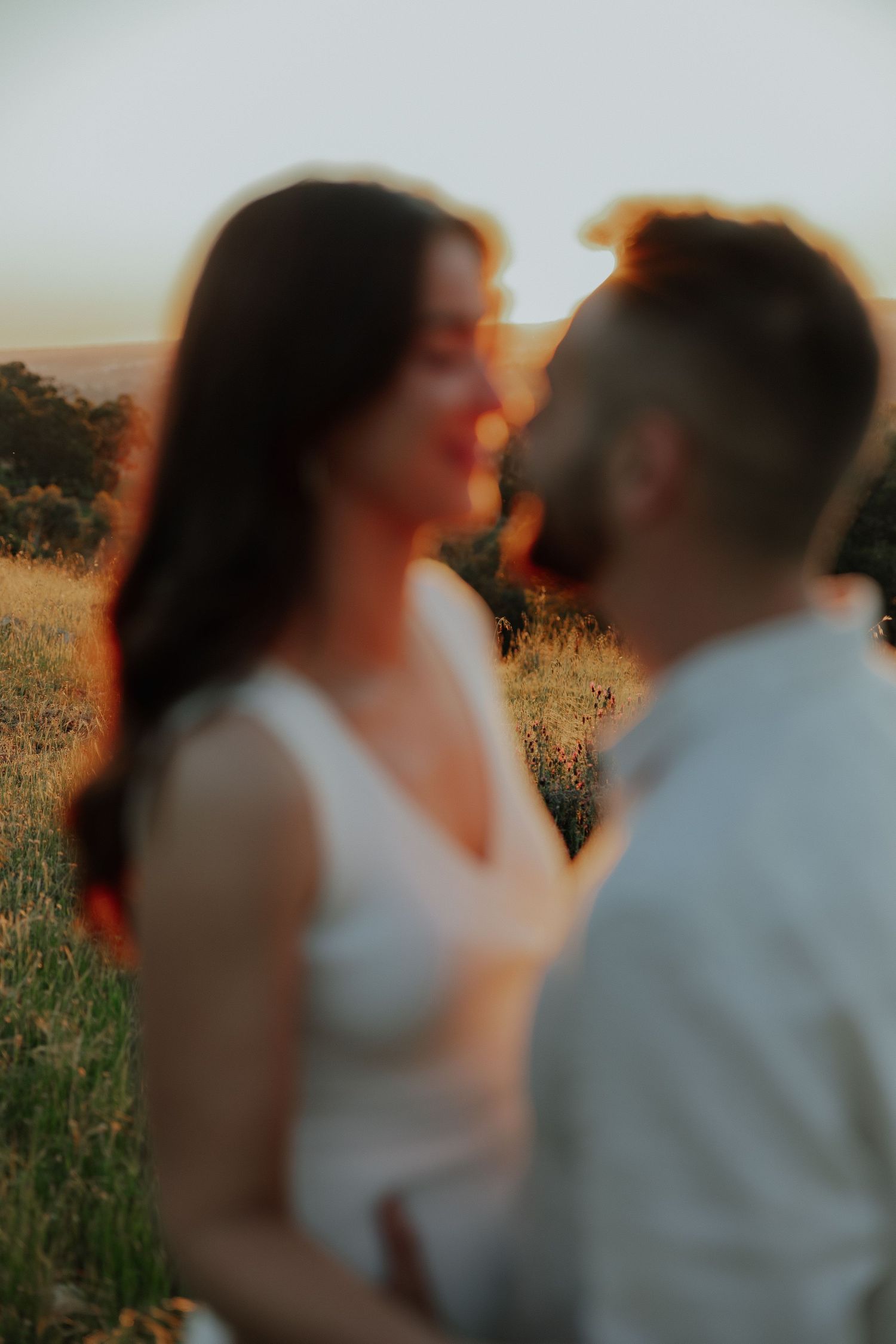 Blurry romantic couple almost kissing at golden sunset in a field, woman in white dress.